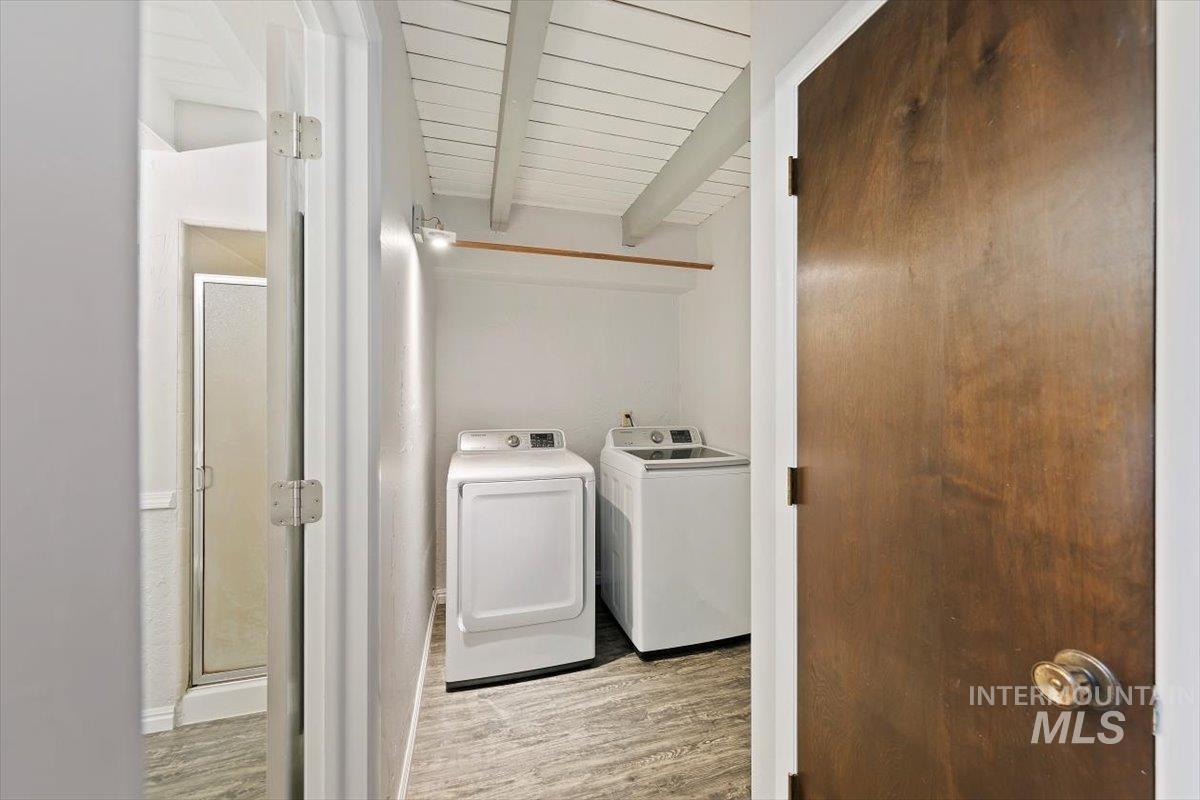 Washroom featuring light wood-style flooring, separate washer and dryer, and a wood ceiling with exposed beams