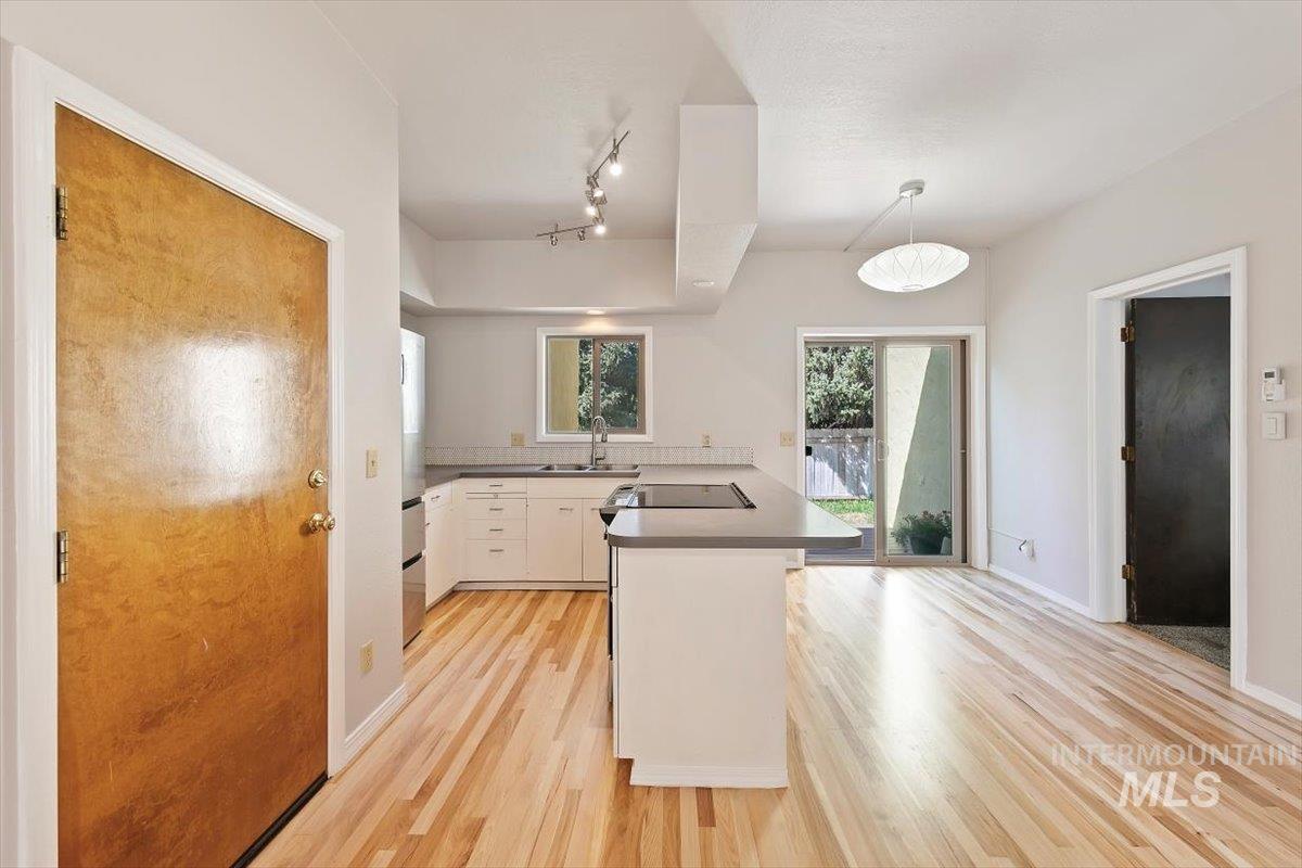 Kitchen with a peninsula, dark countertops, pendant lighting, light wood-type flooring, and white cabinets