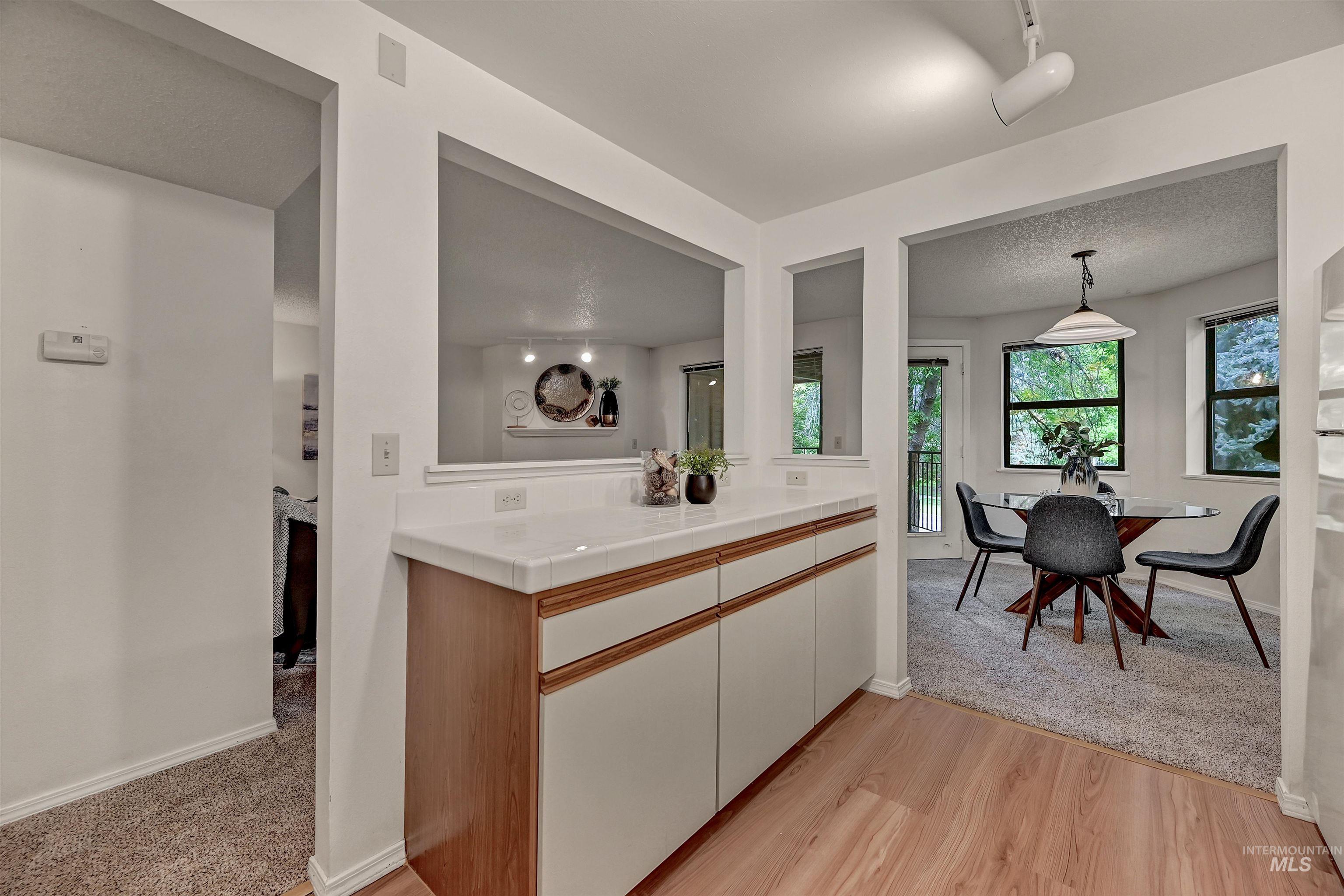 Kitchen featuring tile counters, light wood-type flooring, decorative light fixtures, and light colored carpet