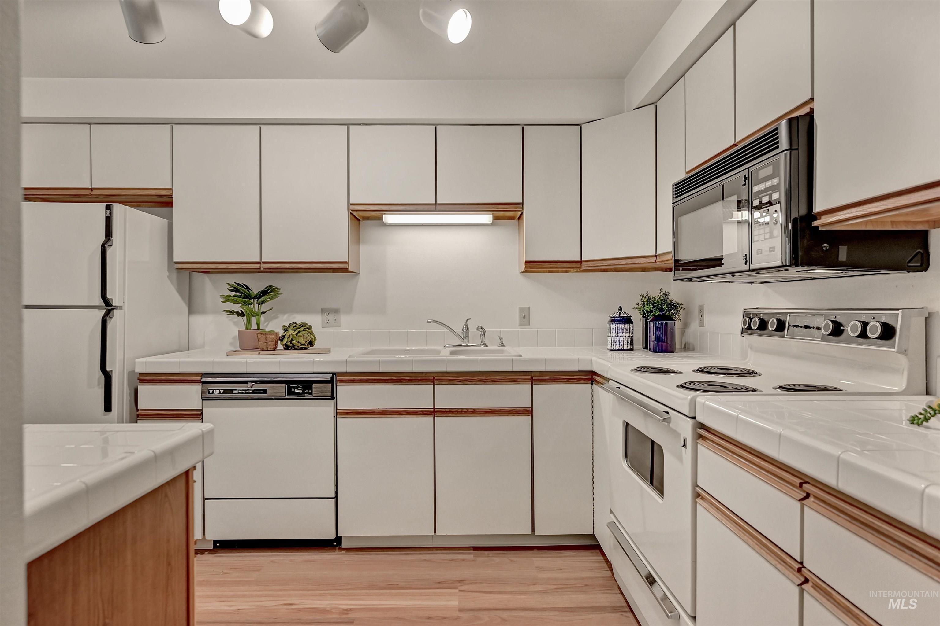 Kitchen featuring white appliances, tile countertops, light wood-type flooring, and brown cabinets
