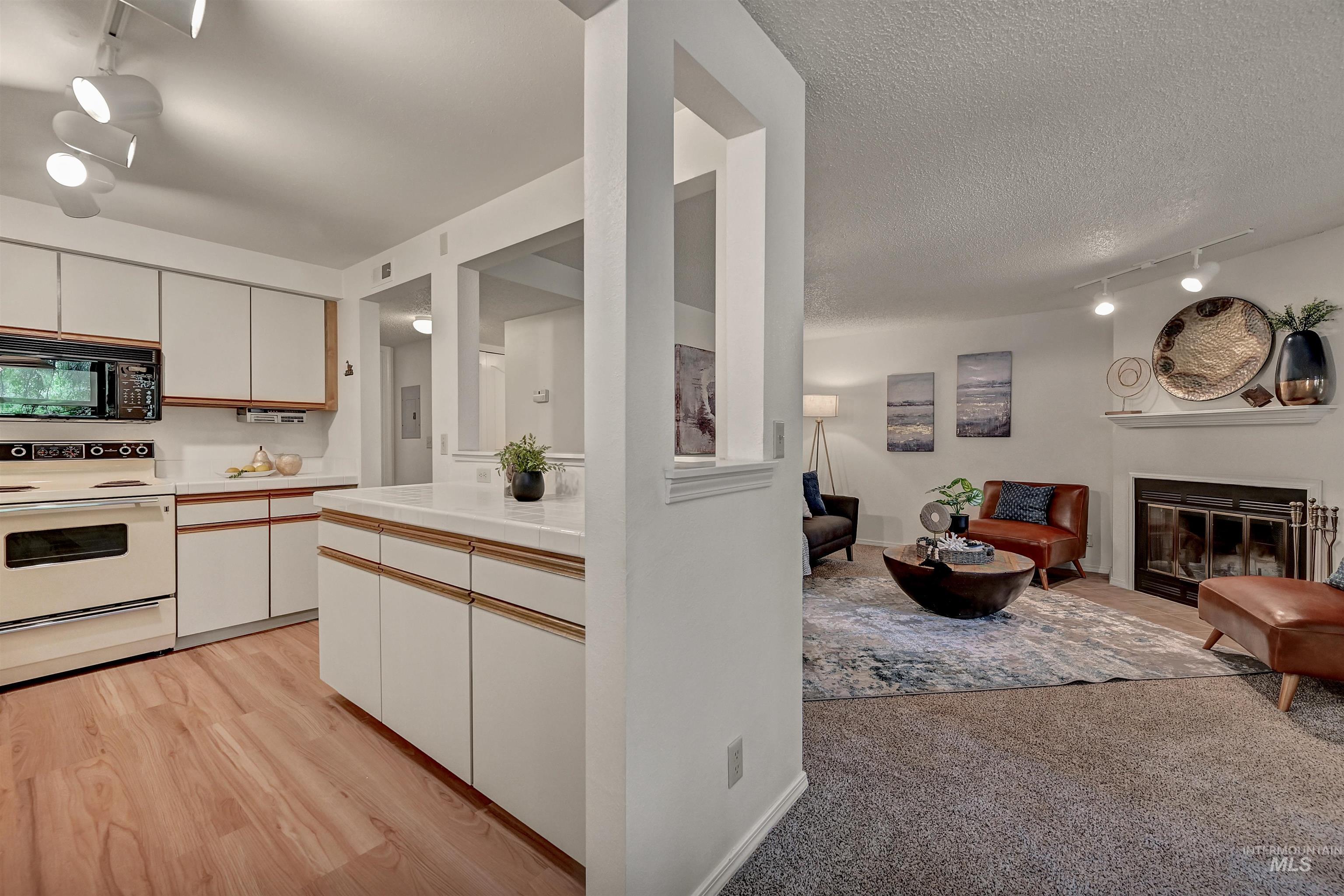 Kitchen featuring track lighting, white electric stove, white cabinets, black microwave, and a glass covered fireplace