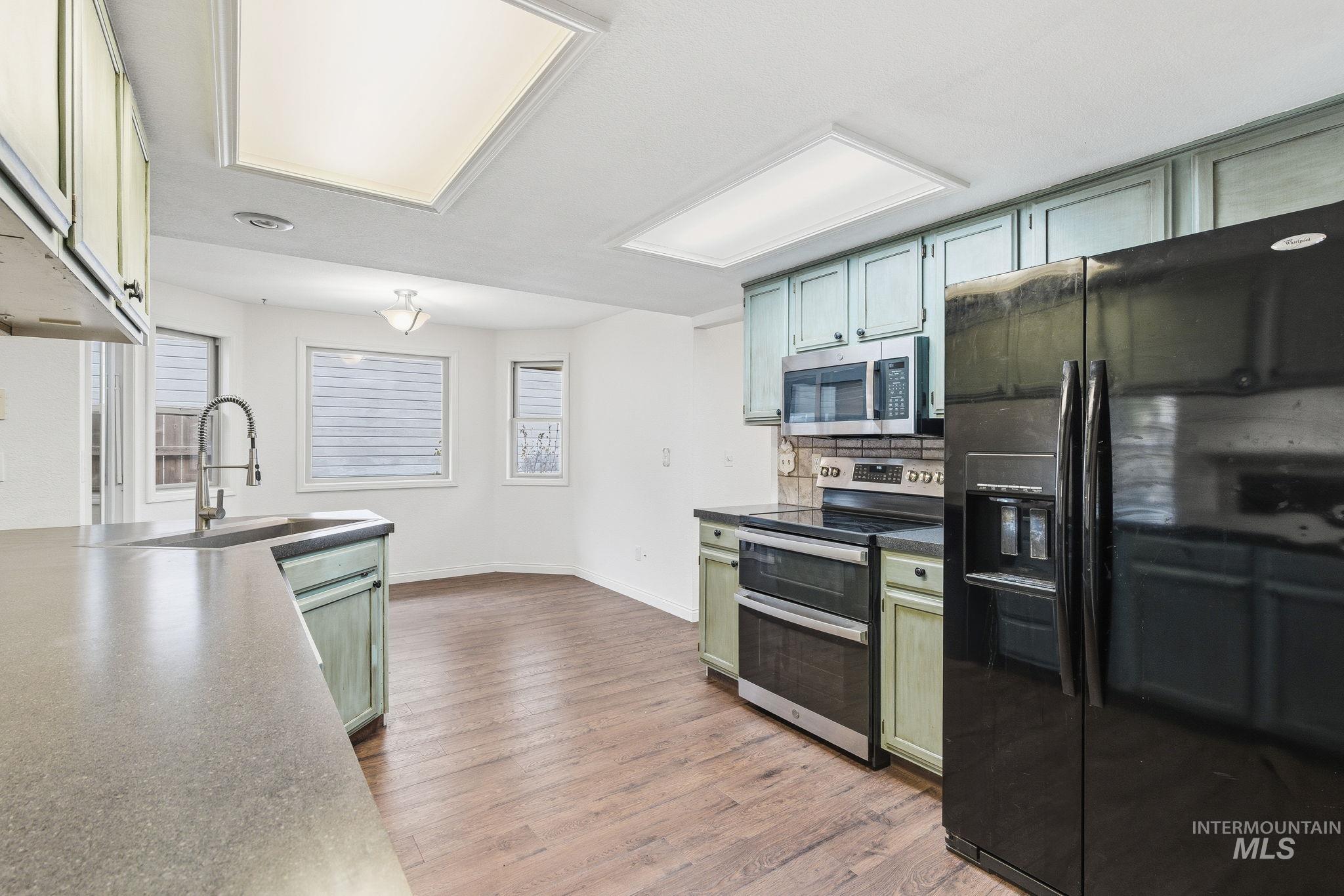 Kitchen with green cabinets, appliances with stainless steel finishes, light wood finished floors, and dark countertops
