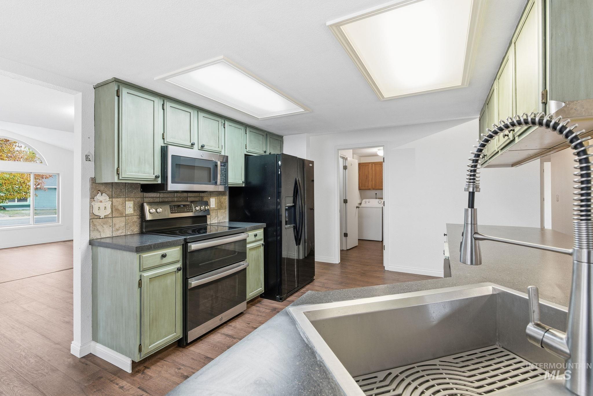 Kitchen with green cabinets, stainless steel appliances, dark wood-type flooring, tasteful backsplash, and washer / dryer