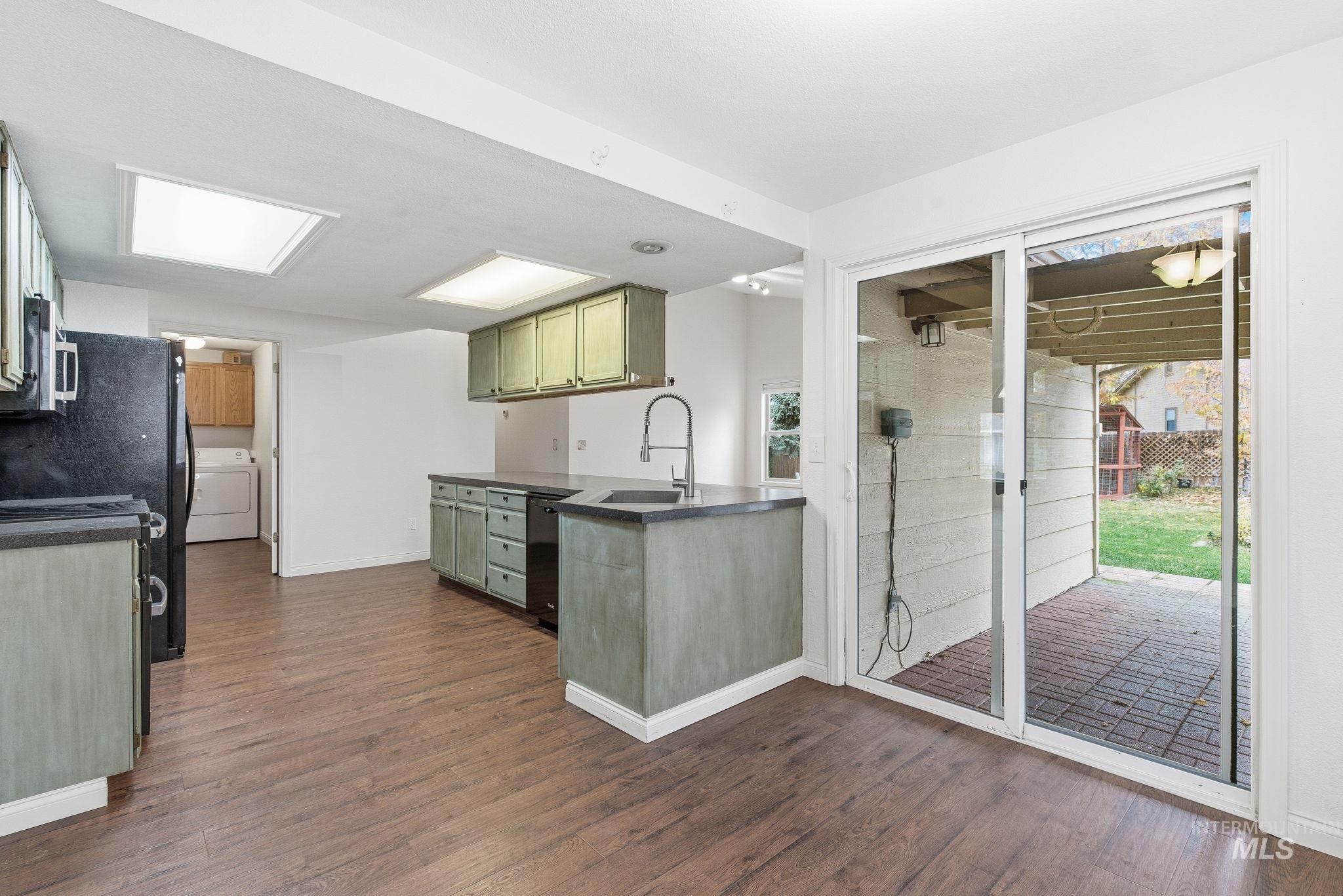 Kitchen with green cabinetry, range, dark wood-style flooring, and washer / clothes dryer