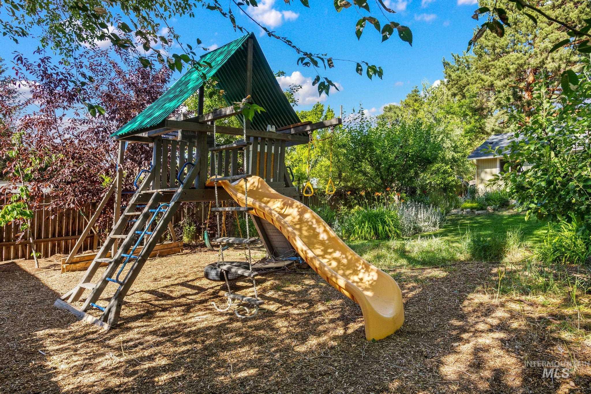 Backyard play structure featuring a green corrugated roof and a yellow slide