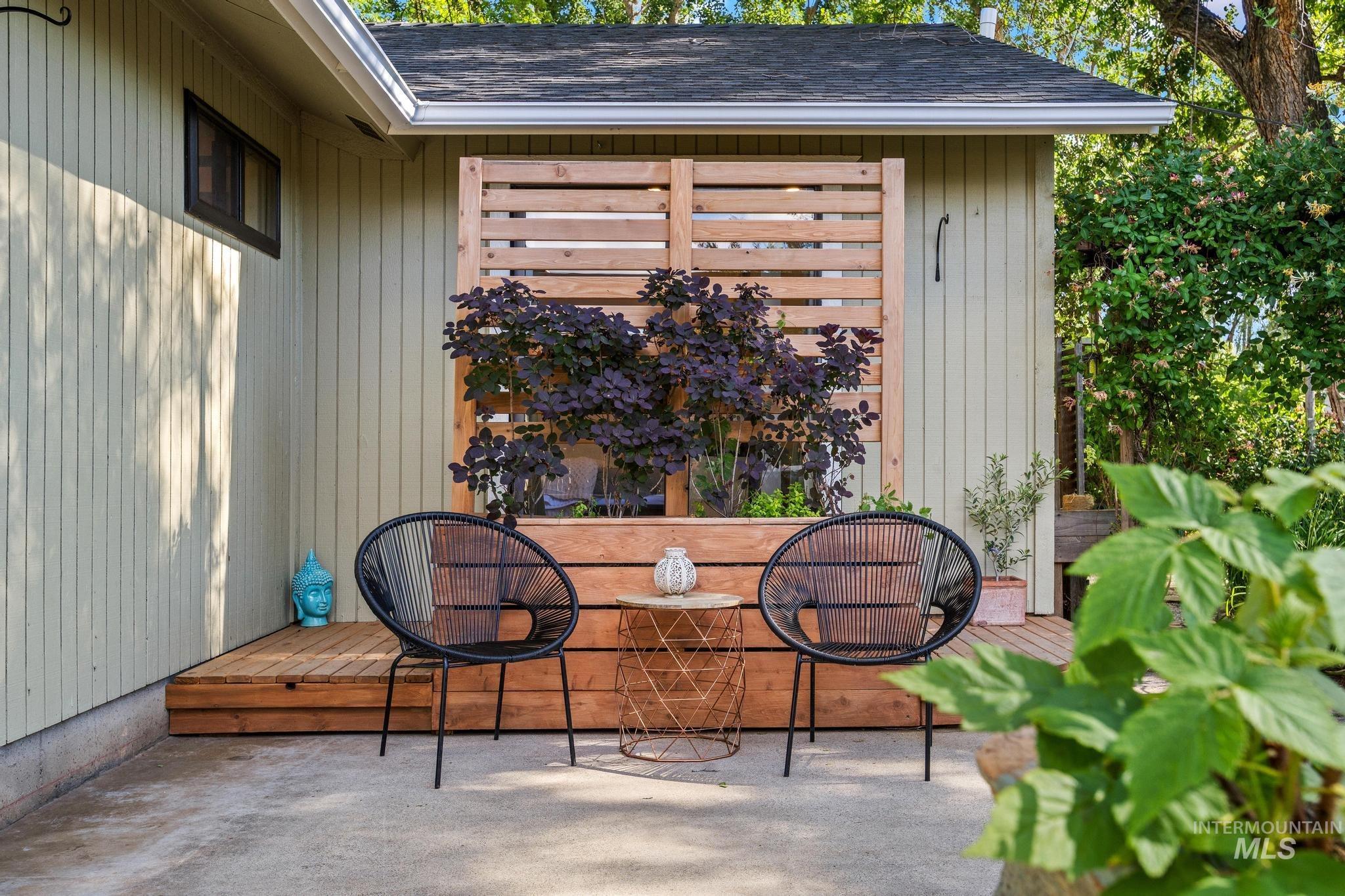Outdoor seating area featuring a wood-plank deck, concrete patio, slatted wood privacy screen, built-in planter with foliage, and vertical siding