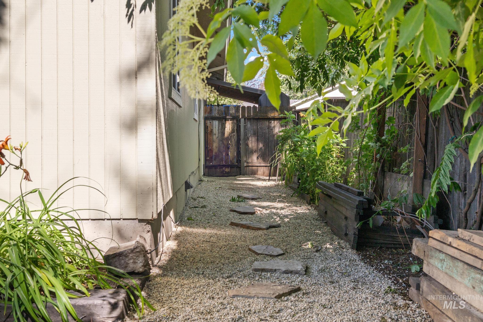 Gravel pathway with stepping stones, bordered by a wooden fence and raised planters