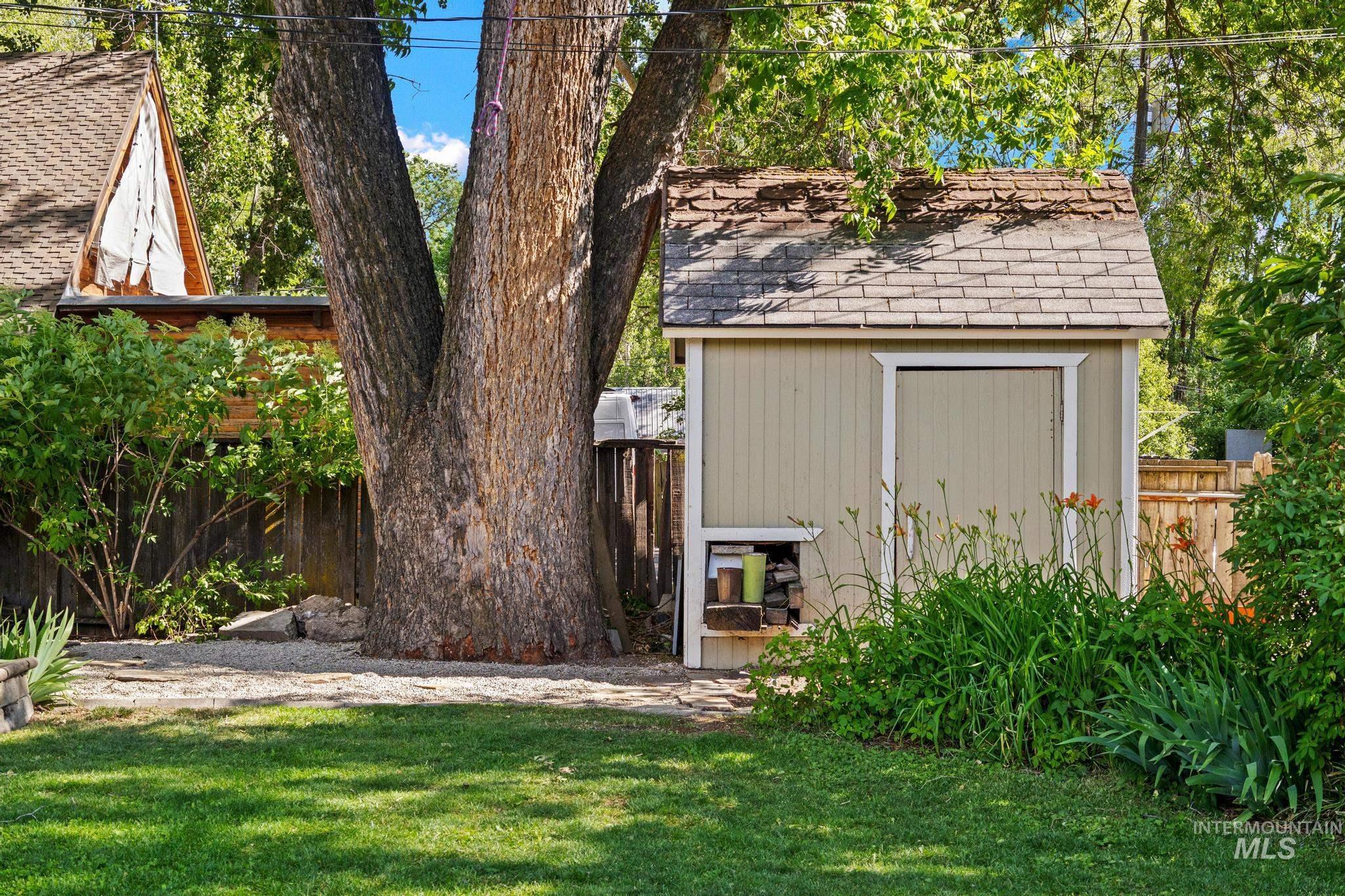 Expansive green lawn featuring a dedicated storage shed with a shingled roof, a mature tree, and a wooden privacy fence
