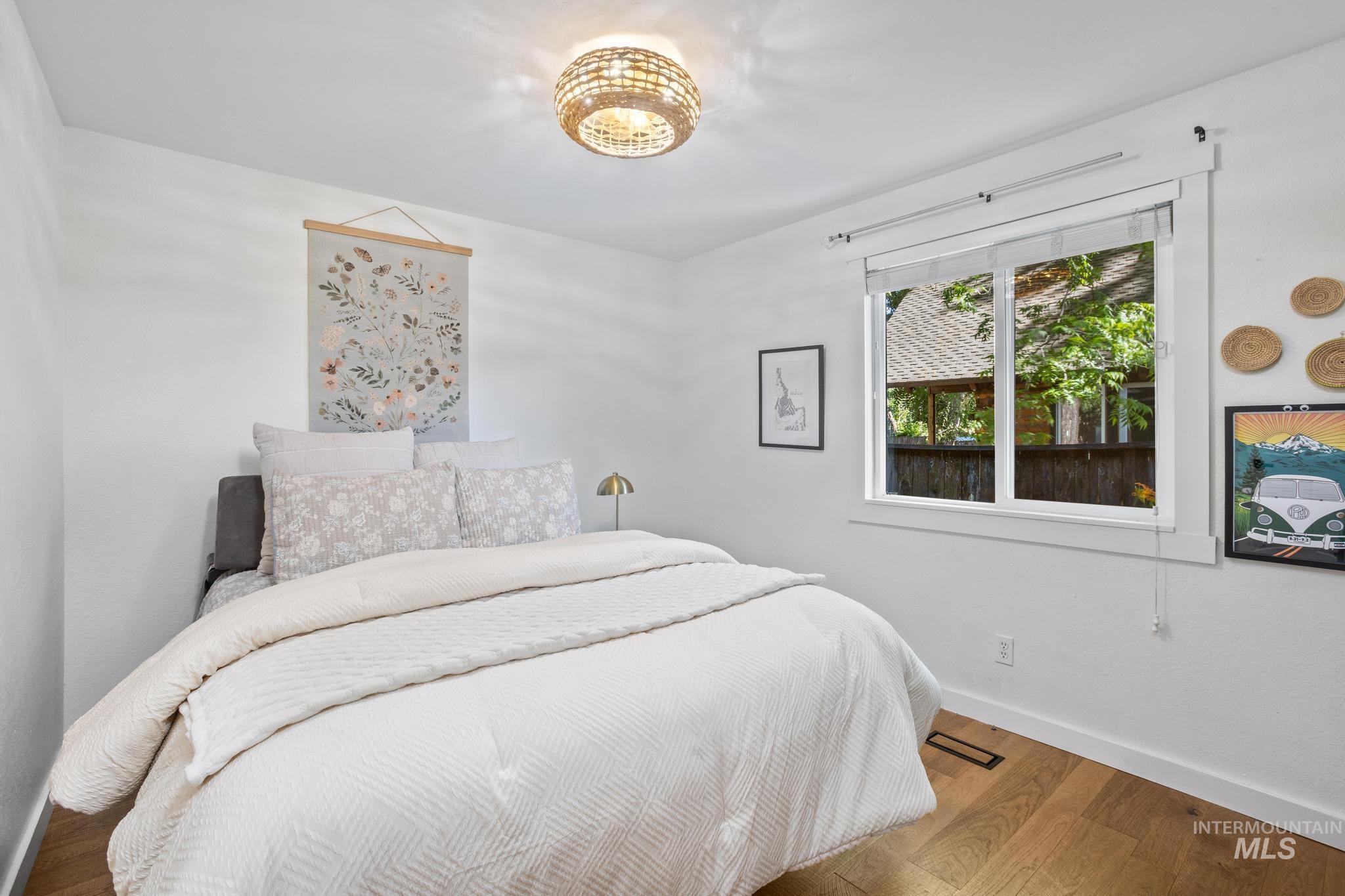 Bedroom featuring wood-finish flooring, a window with exterior views, and a woven flush-mount ceiling light