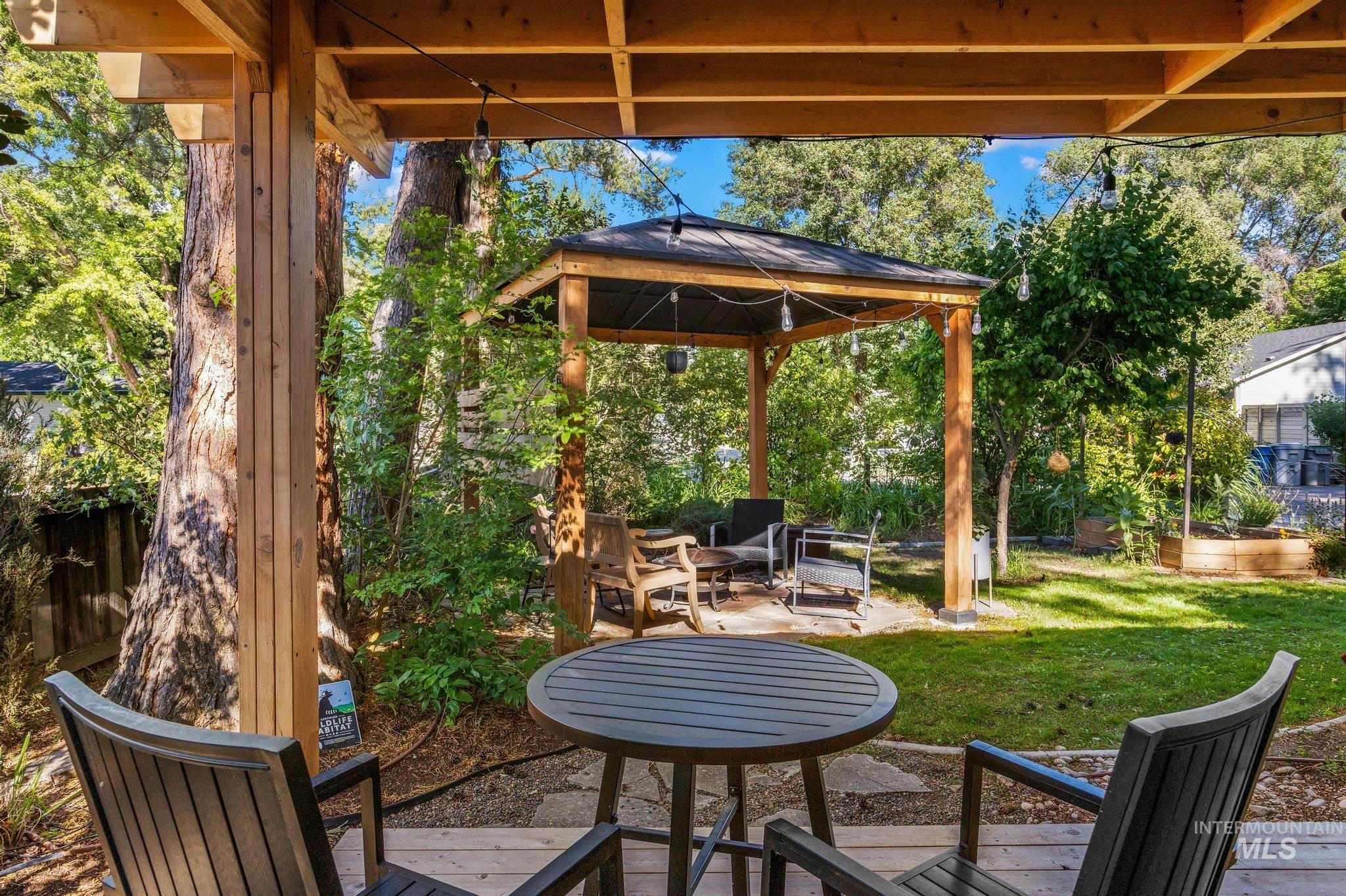 Spacious outdoor living area featuring a wooden pergola, string lighting, and a separate wood-framed gazebo with a dark roof
