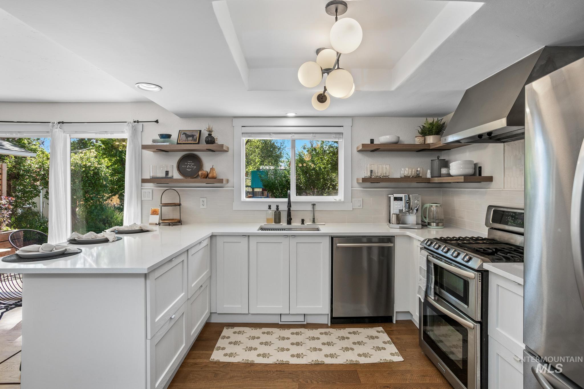 L-shaped kitchen featuring white cabinetry, light countertops, wood-finish flooring, a stainless steel gas range with a double oven, and a built-in stainless steel dishwasher