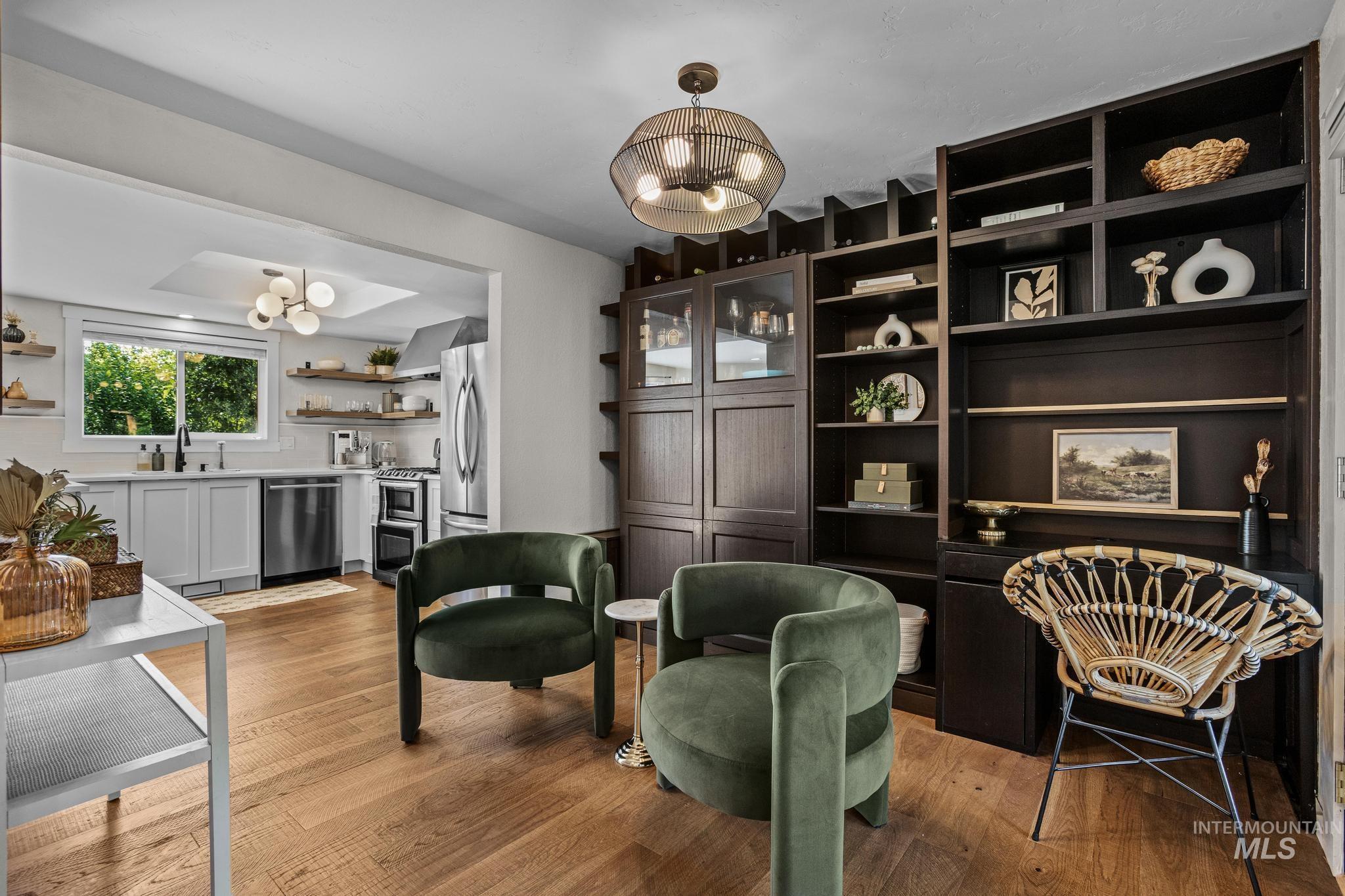 Open-concept living space featuring wood-finish flooring, a built-in dark wood shelving unit, and a kitchen with light cabinetry, stainless steel appliances, and a window