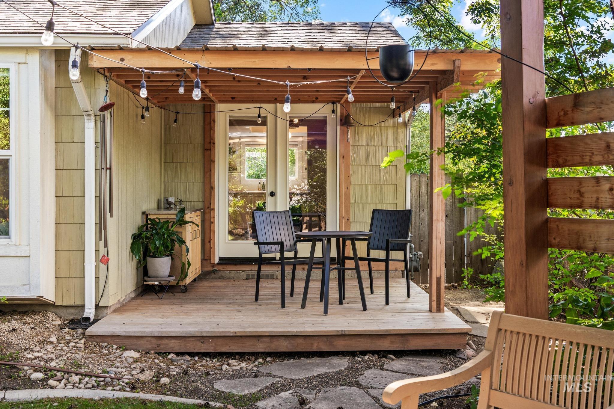 Wood-finish deck with a pergola, string lighting, and direct access to the interior through glass-paneled double doors