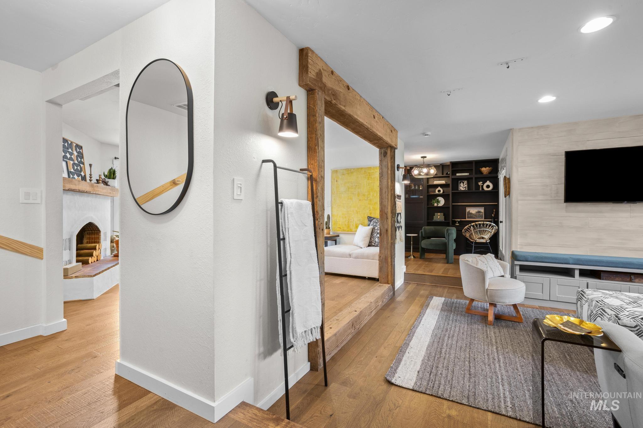 Open-concept living space featuring wood-finish flooring, a built-in entertainment center with integrated bench seating, and a beamed doorway leading to an additional living area