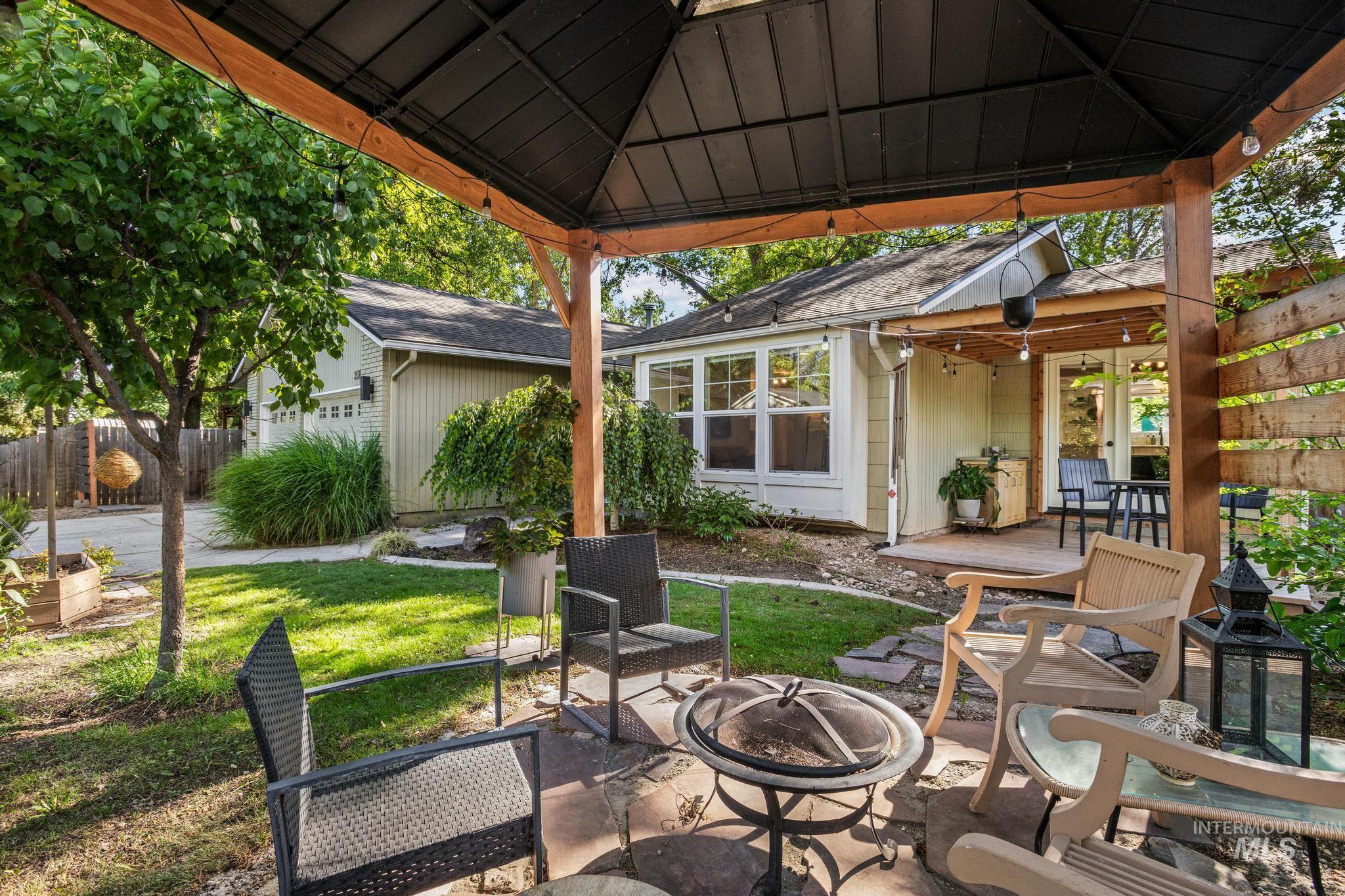 Covered outdoor patio area featuring a stone paver base, a black metal gazebo with wood frame, and string lighting