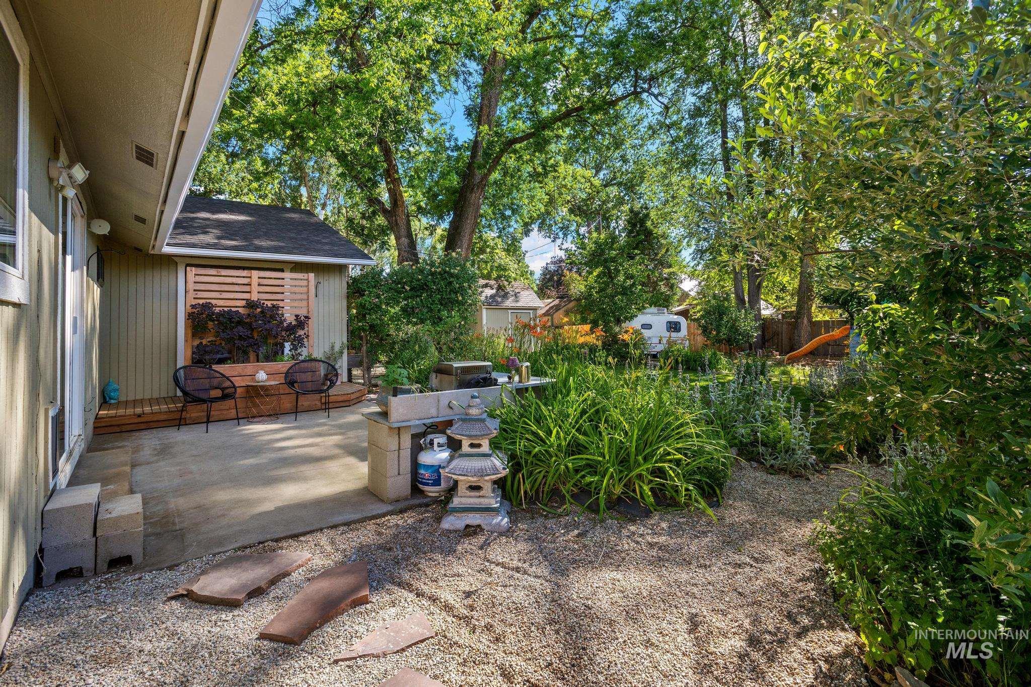 Expansive backyard featuring a concrete patio, gravel pathways, mature trees, and established plantings