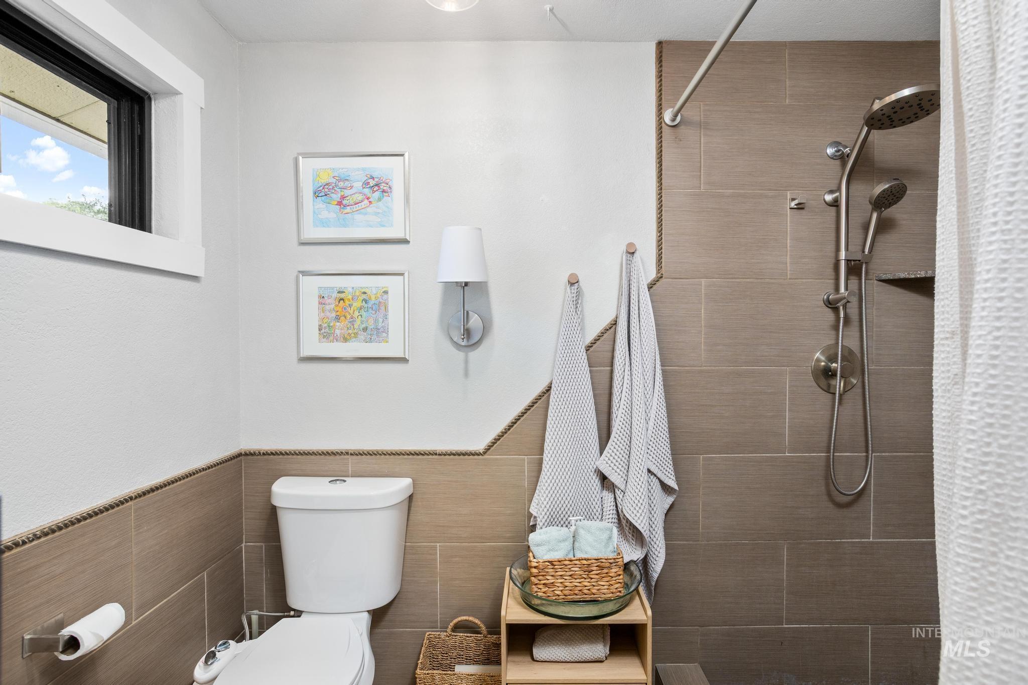 Bathroom featuring a tiled shower surround, a wall-mounted showerhead with a handheld sprayer, an integrated shower shelf, and a window with white trim