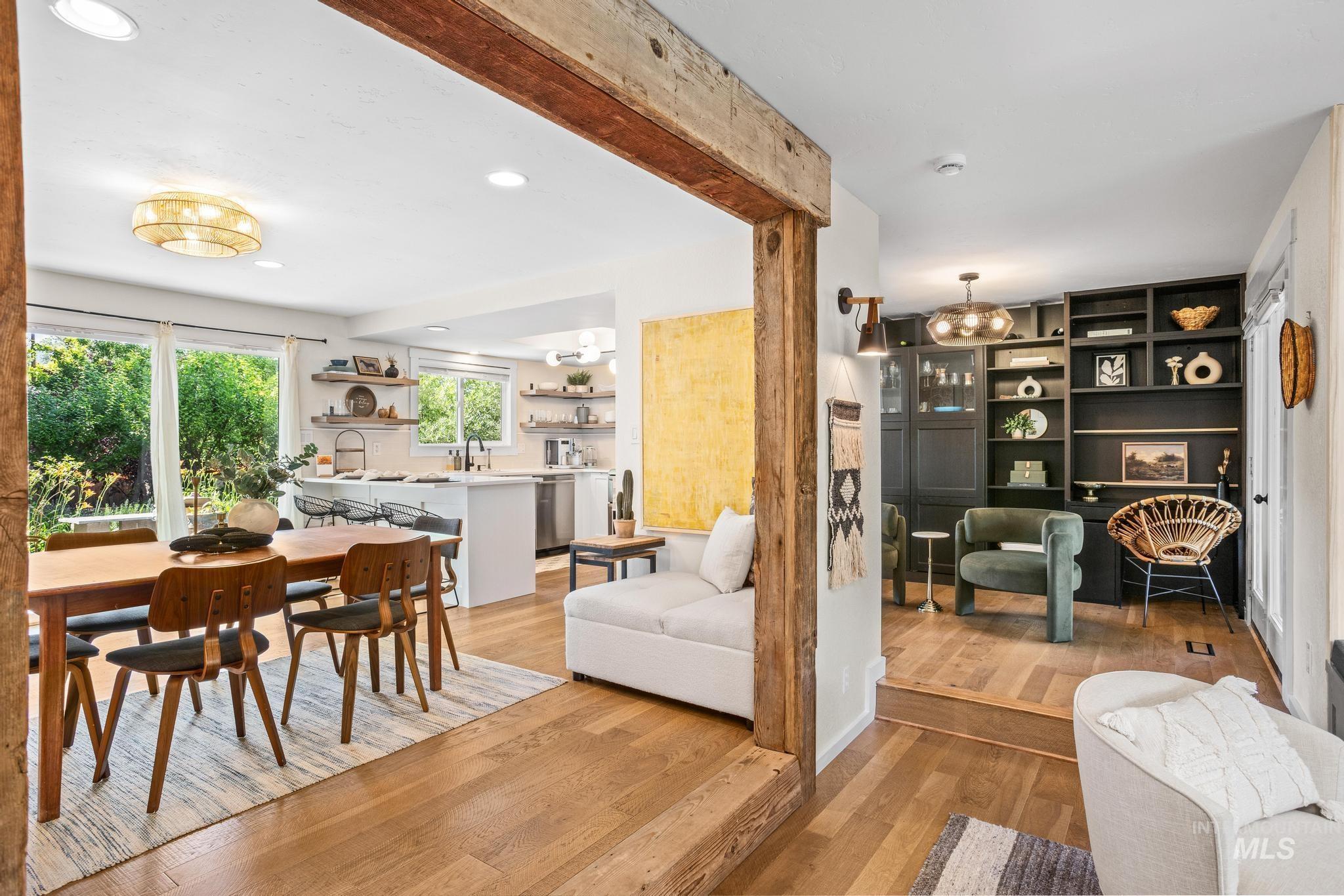 Open concept living space featuring wood-finish flooring, exposed wood beam accents, recessed lighting, and a modern kitchen with a white island and stainless steel appliances