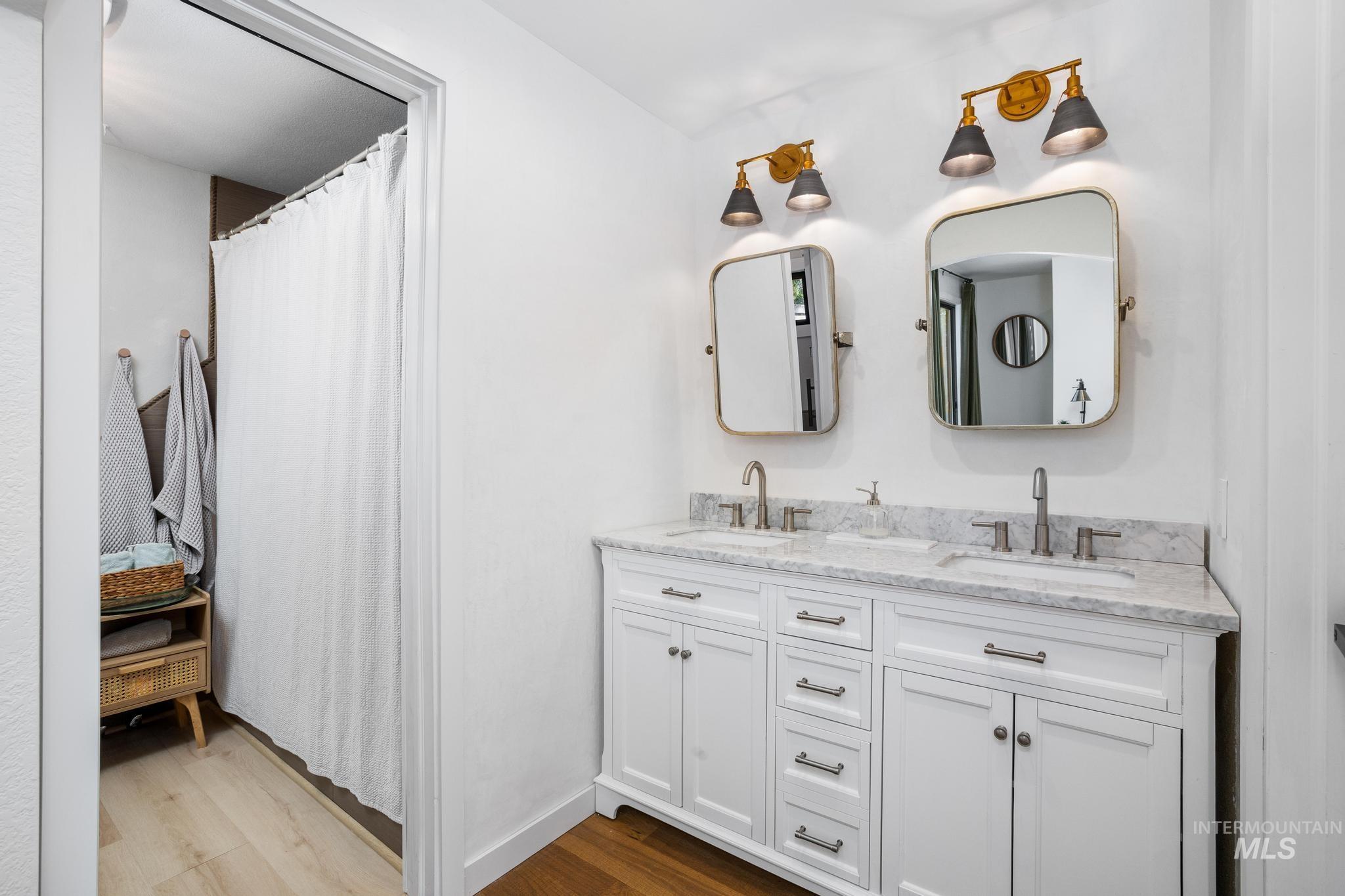Dual vanity featuring white cabinetry with brushed nickel hardware, individual rectangular mirrors, and two-light sconce fixtures with brass and black accents