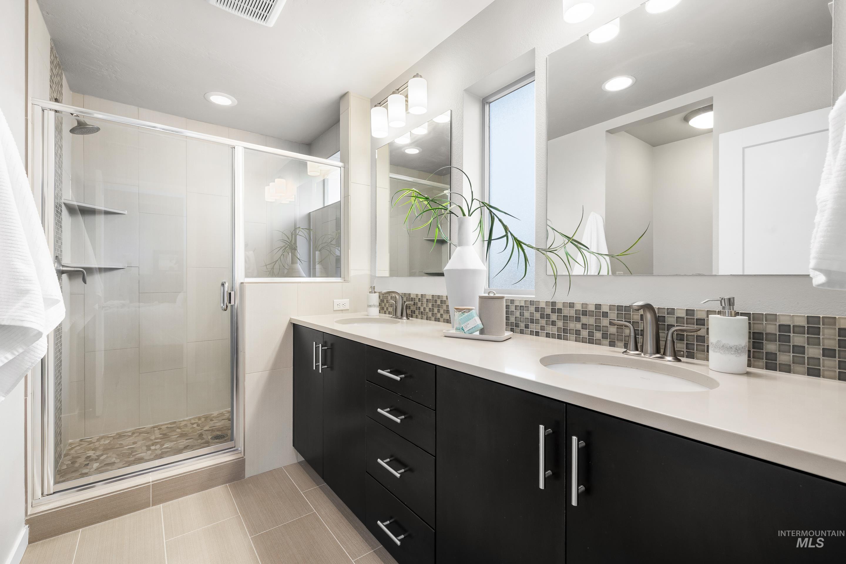 Bathroom featuring double vanity, a stall shower, tasteful backsplash, light tile patterned floors, and recessed lighting