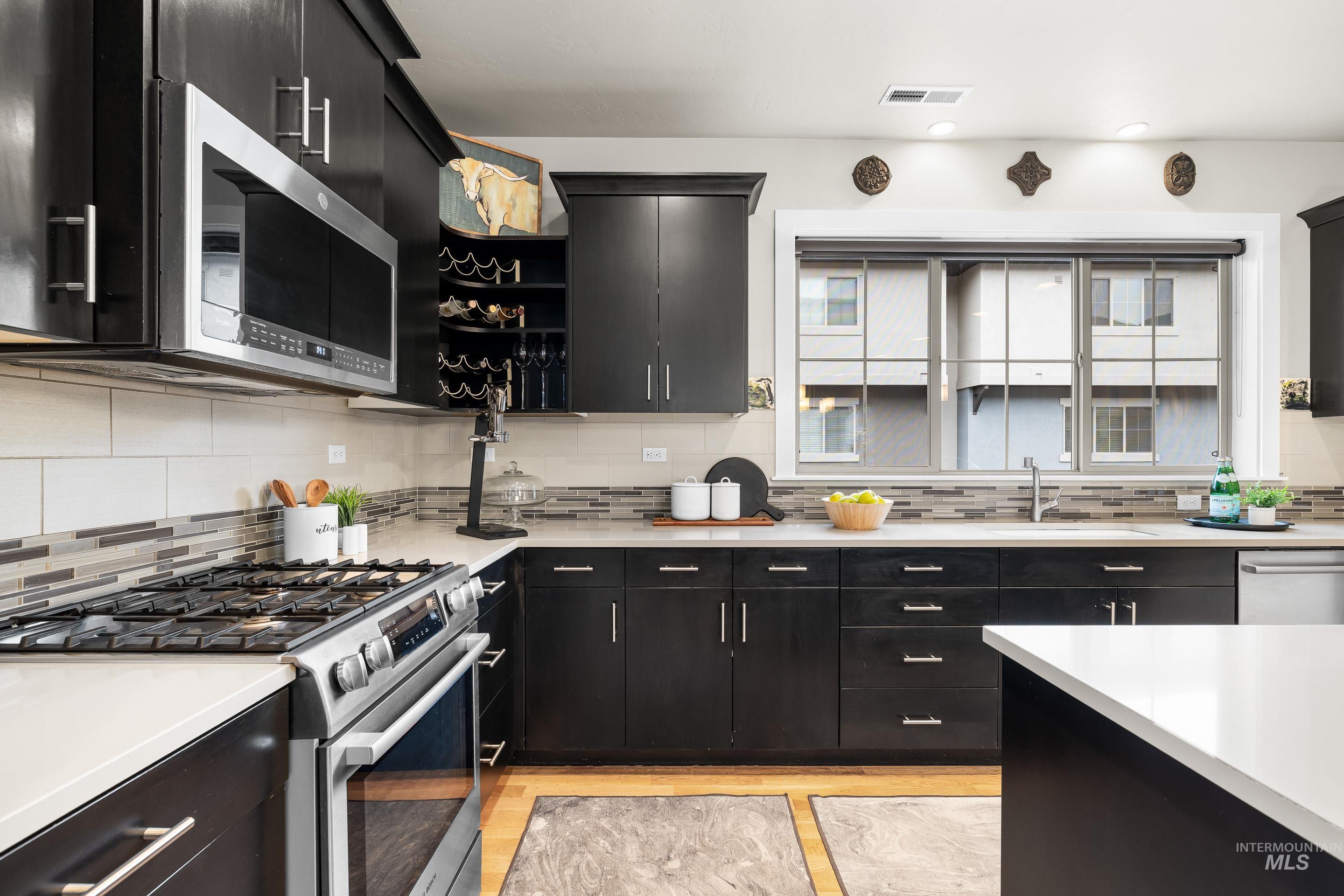 Kitchen featuring dark cabinets, stainless steel appliances, open shelves, and backsplash