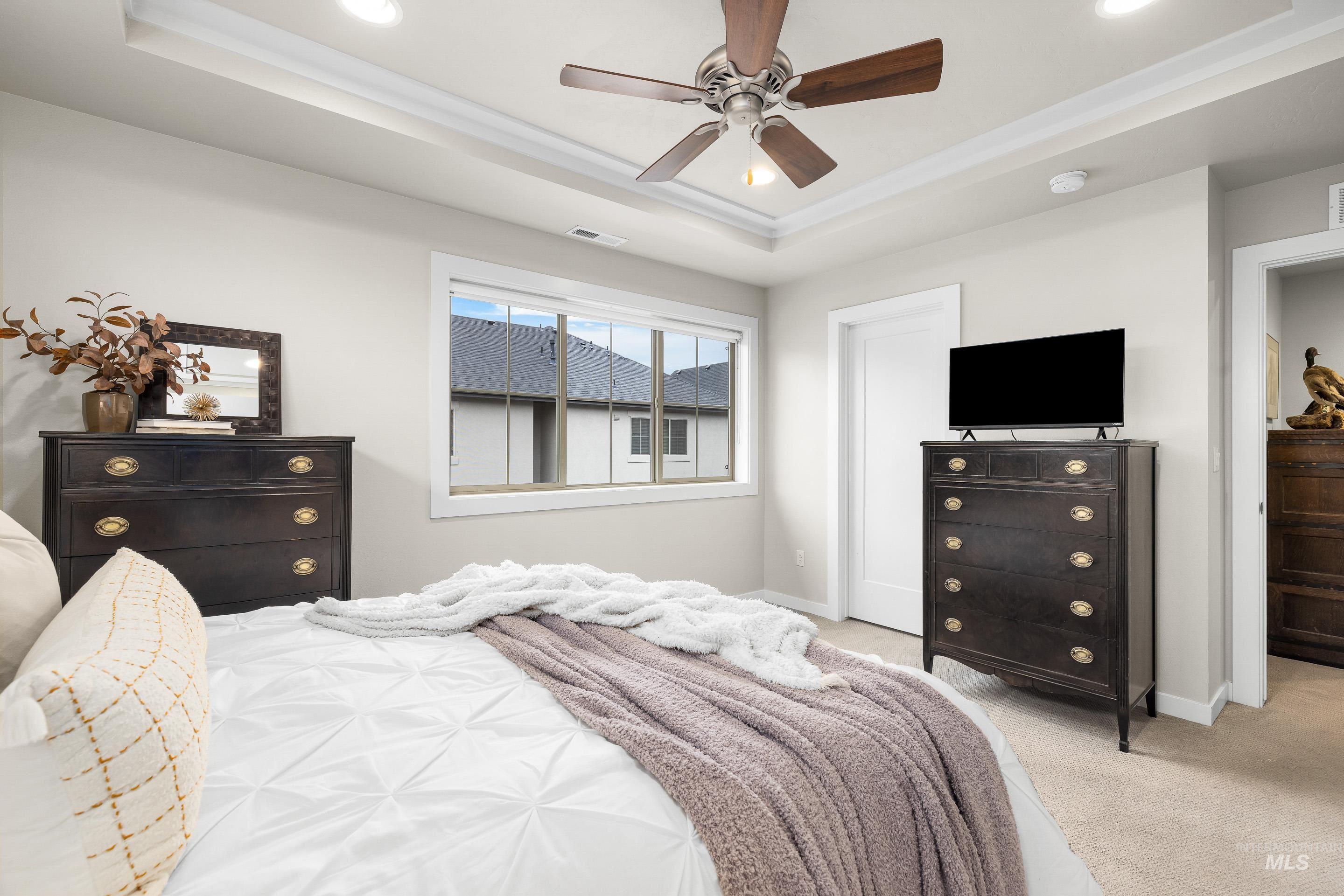 Carpeted bedroom with ceiling fan, recessed lighting, and a tray ceiling
