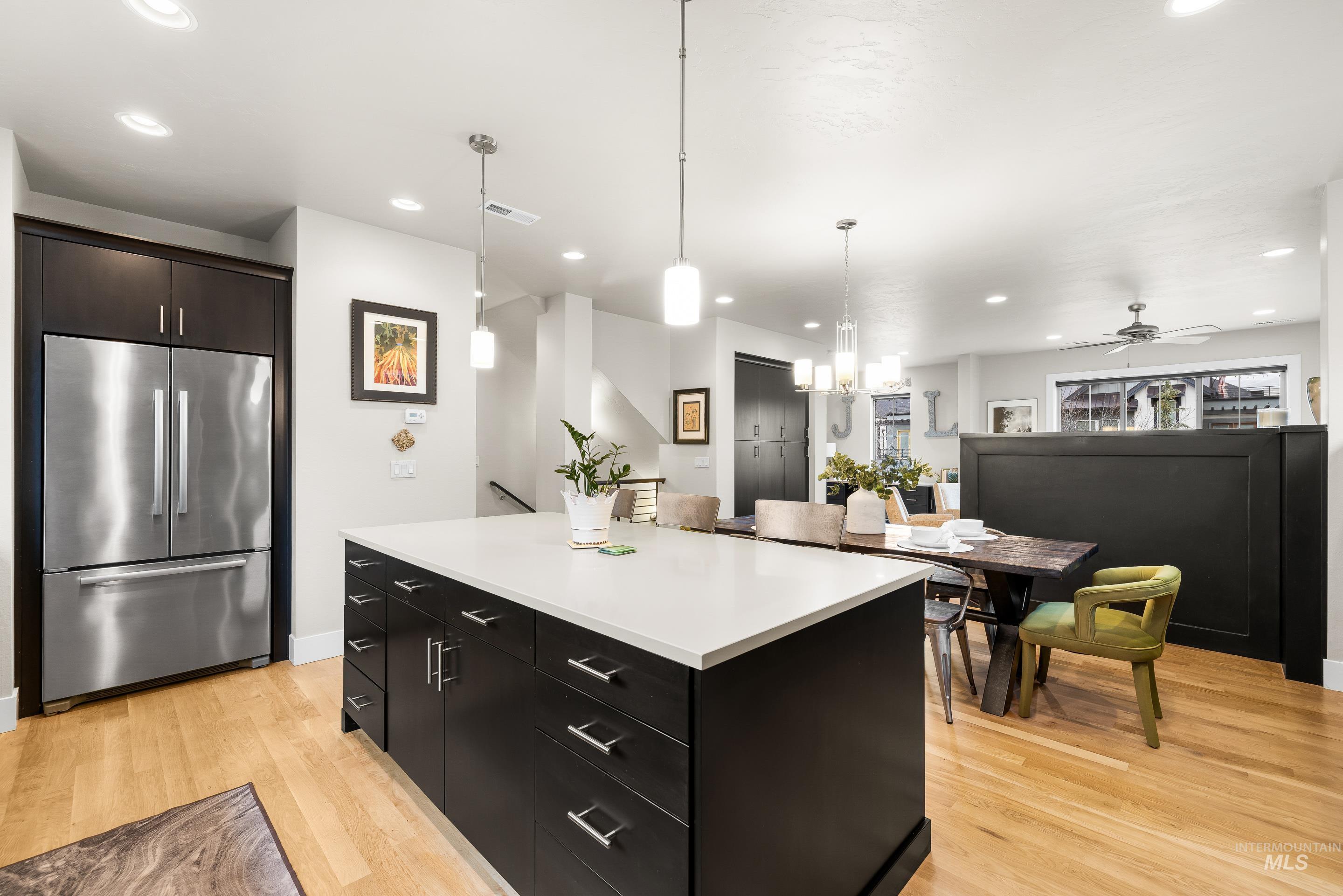 Kitchen with dark cabinetry, freestanding refrigerator, decorative light fixtures, a kitchen island, and light wood-style floors