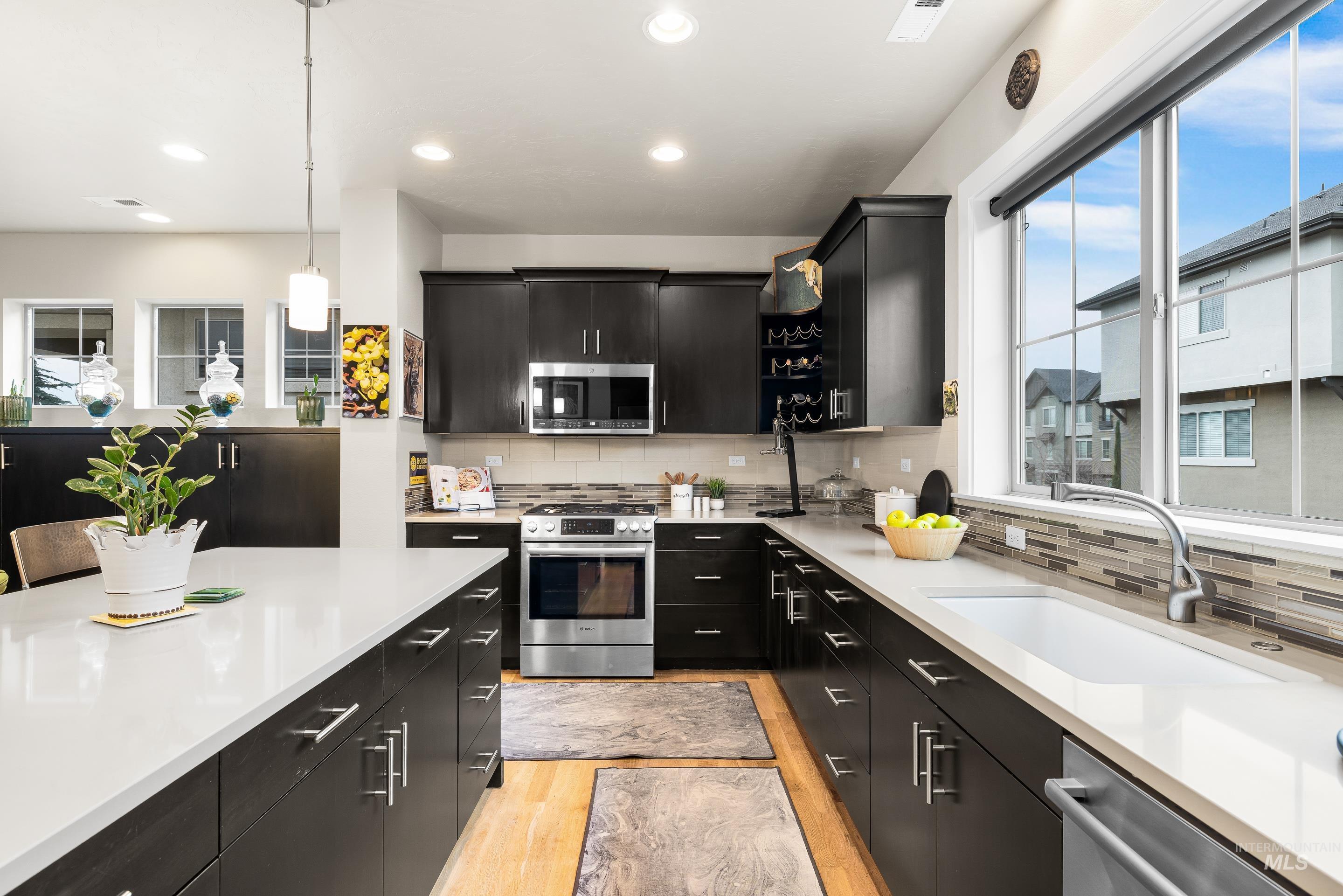 Kitchen with dark cabinets, stainless steel appliances, decorative light fixtures, plenty of natural light, and recessed lighting