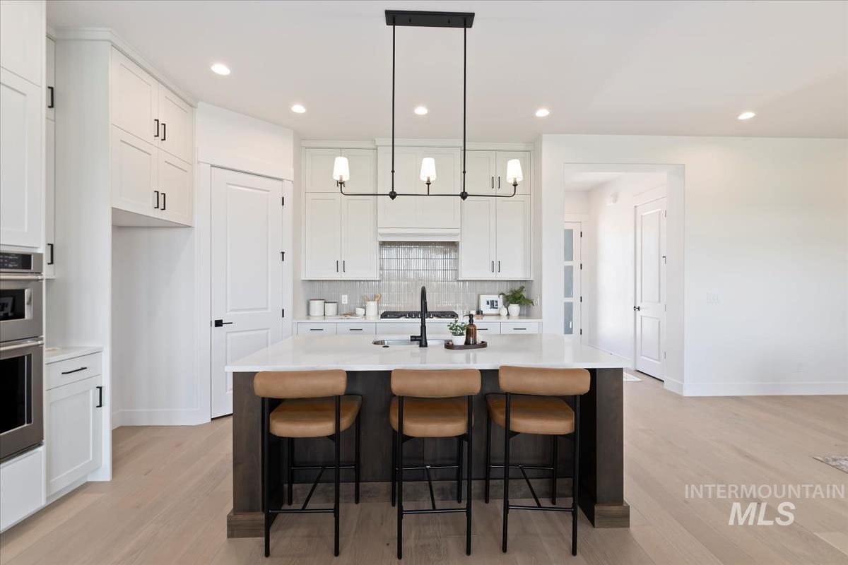 Kitchen featuring hanging light fixtures, white cabinets, a kitchen breakfast bar, backsplash, and an island with sink
