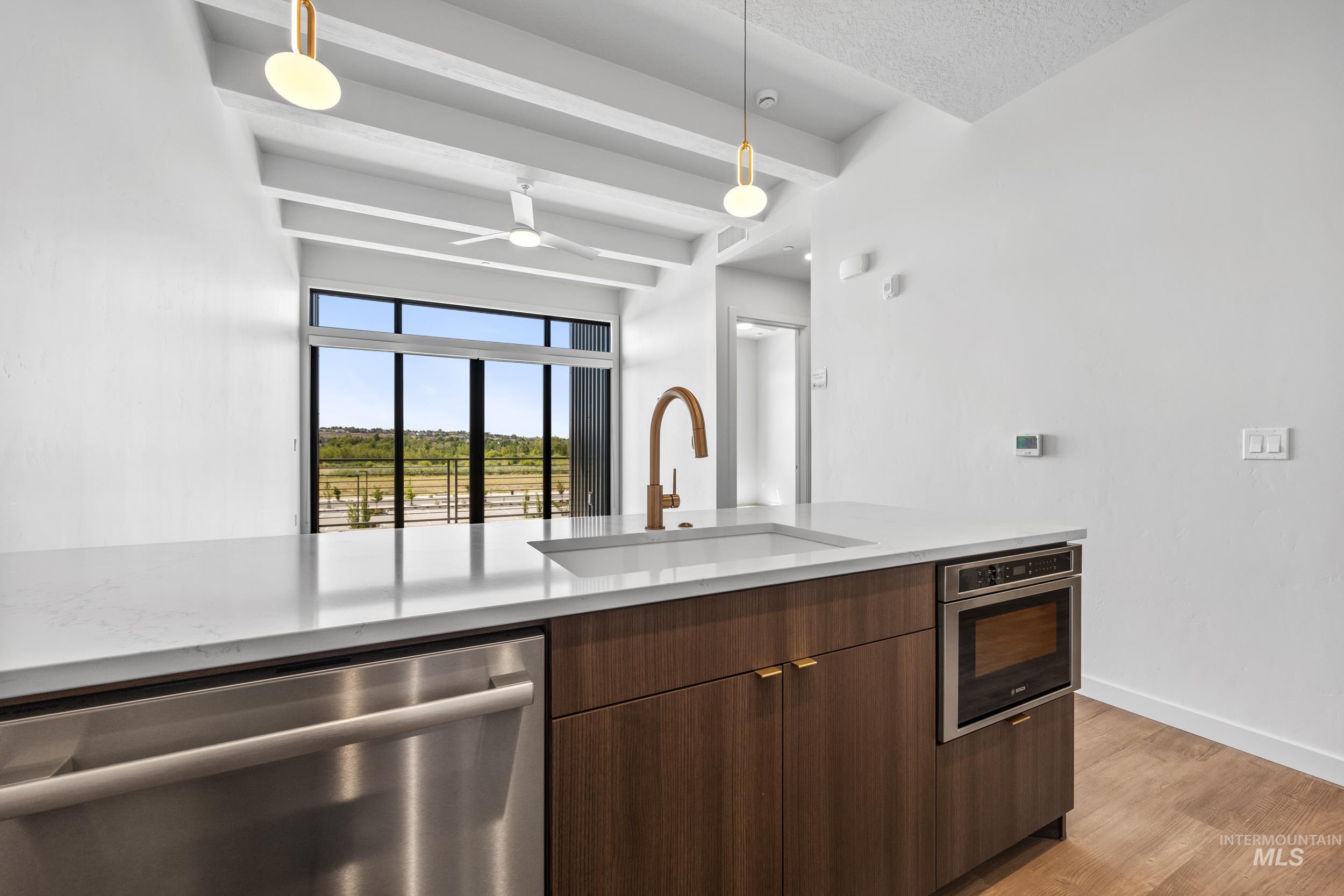 Kitchen with stainless steel appliances, modern cabinets, beam ceiling, decorative light fixtures, and light wood-type flooring