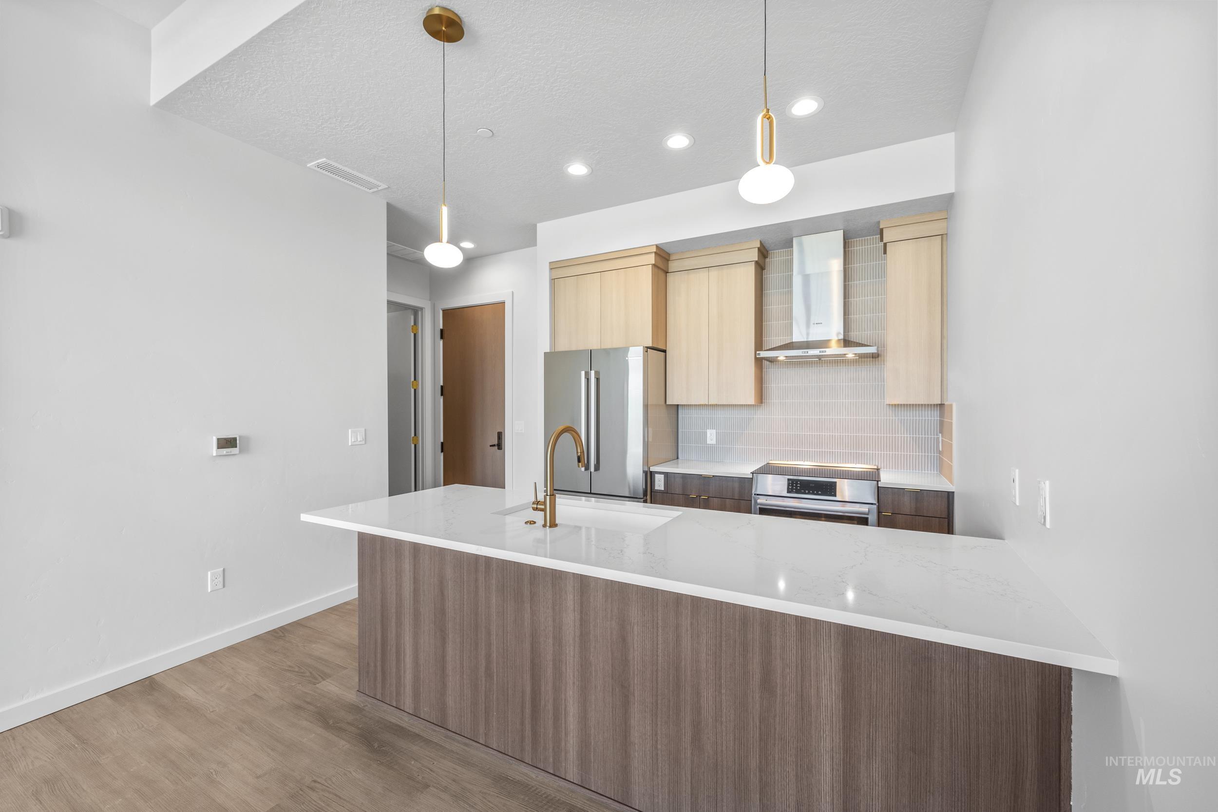 Kitchen featuring modern cabinets, tasteful backsplash, wall chimney range hood, light stone countertops, and light wood-style floors