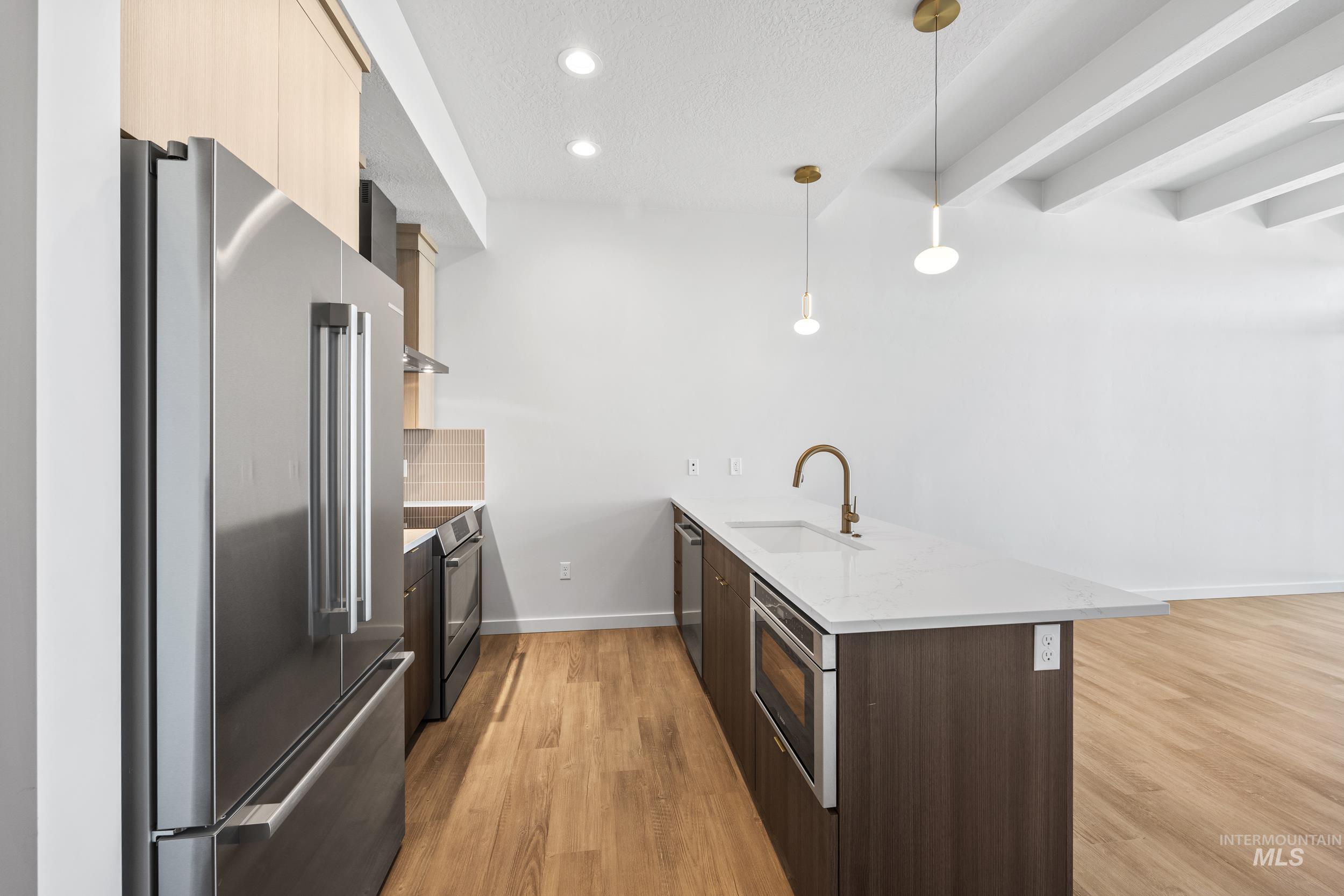 Kitchen featuring modern cabinets, a peninsula, appliances with stainless steel finishes, light stone countertops, and light wood finished floors