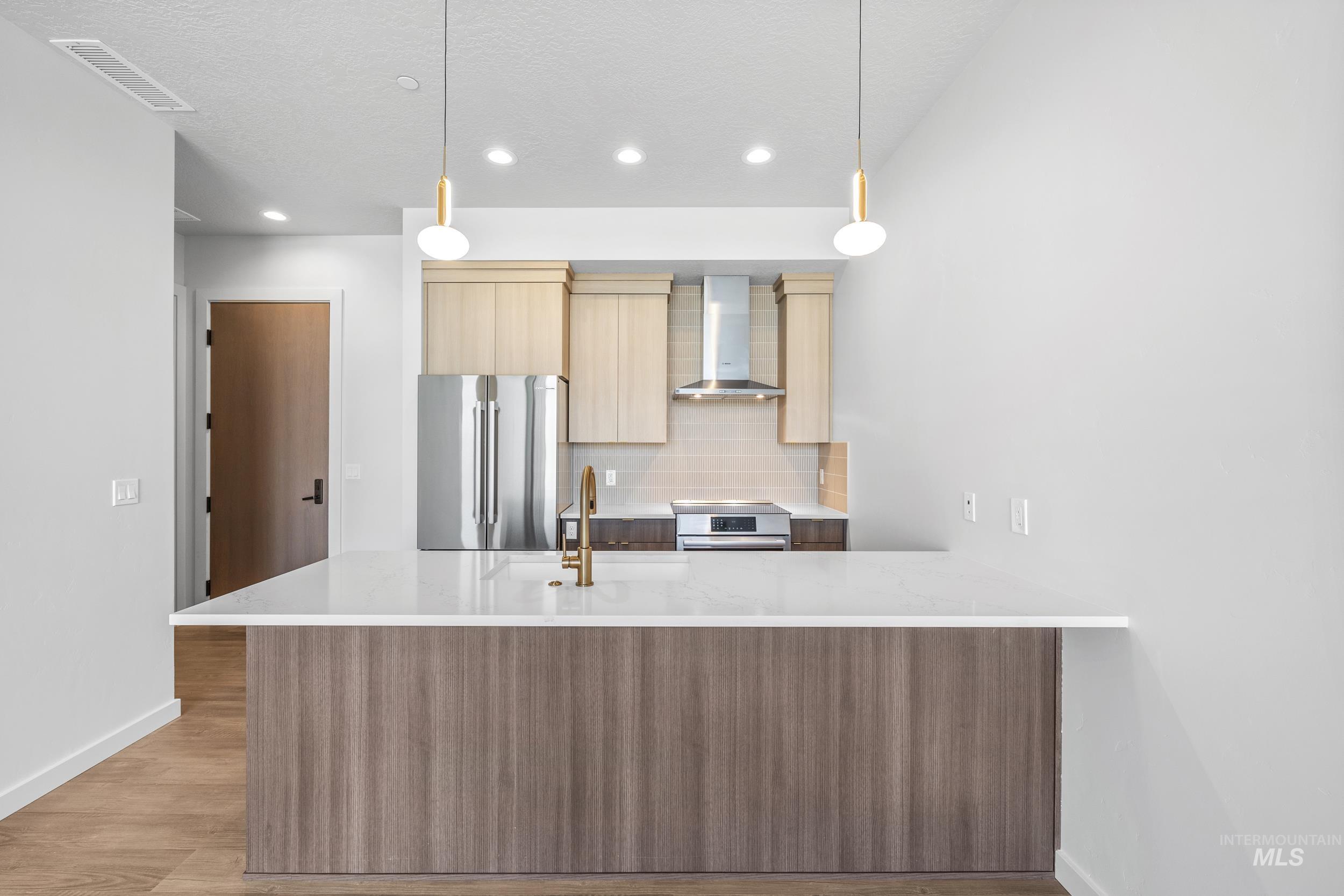 Kitchen with modern cabinets, decorative backsplash, wall chimney exhaust hood, appliances with stainless steel finishes, and light stone countertops