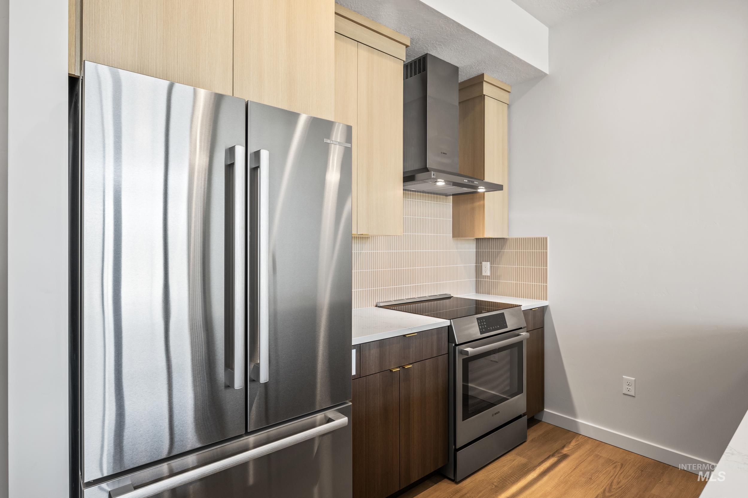 Kitchen featuring modern cabinets, appliances with stainless steel finishes, dark wood-style flooring, wall chimney range hood, and backsplash
