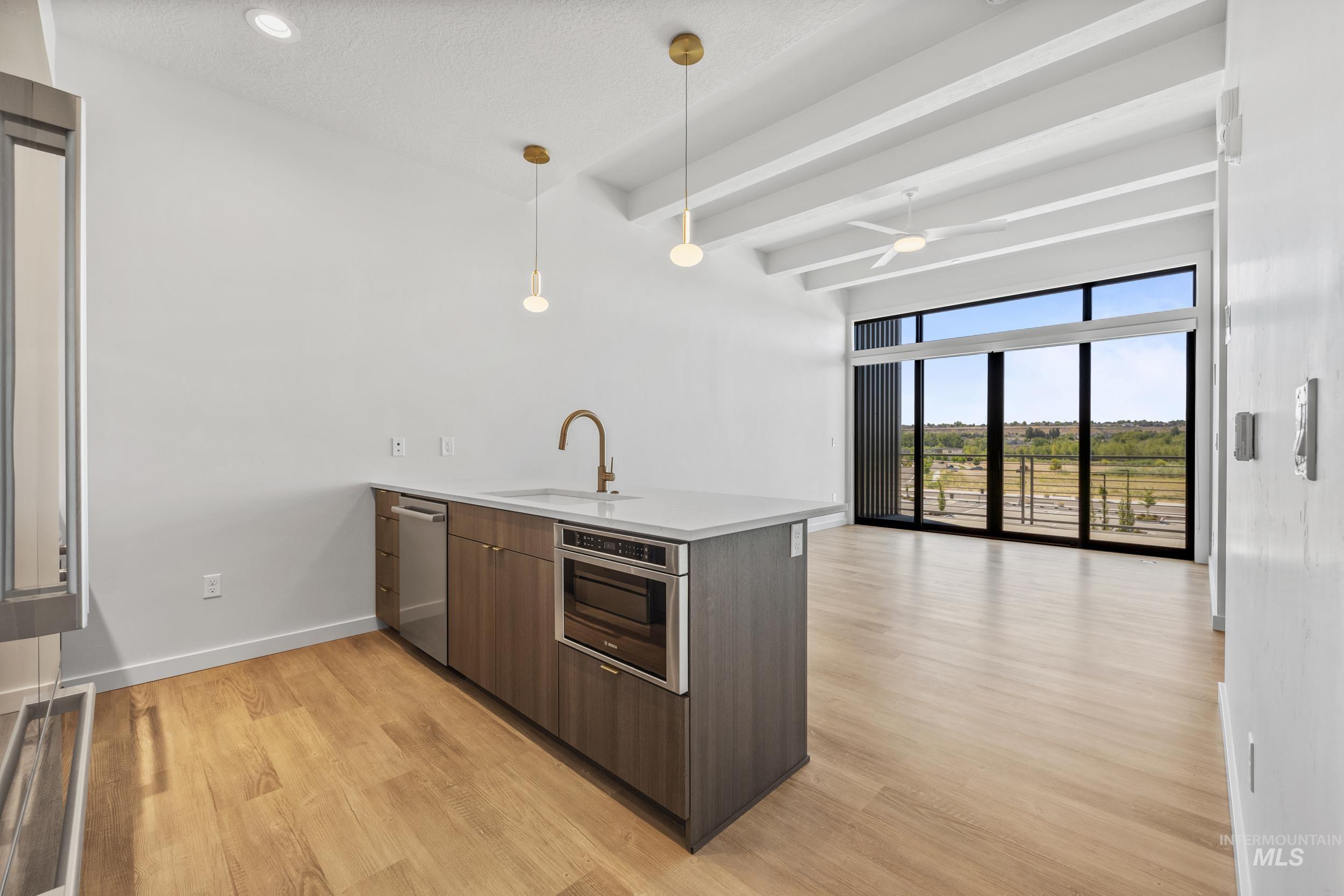 Kitchen featuring a peninsula, modern cabinets, beam ceiling, light wood finished floors, and decorative light fixtures