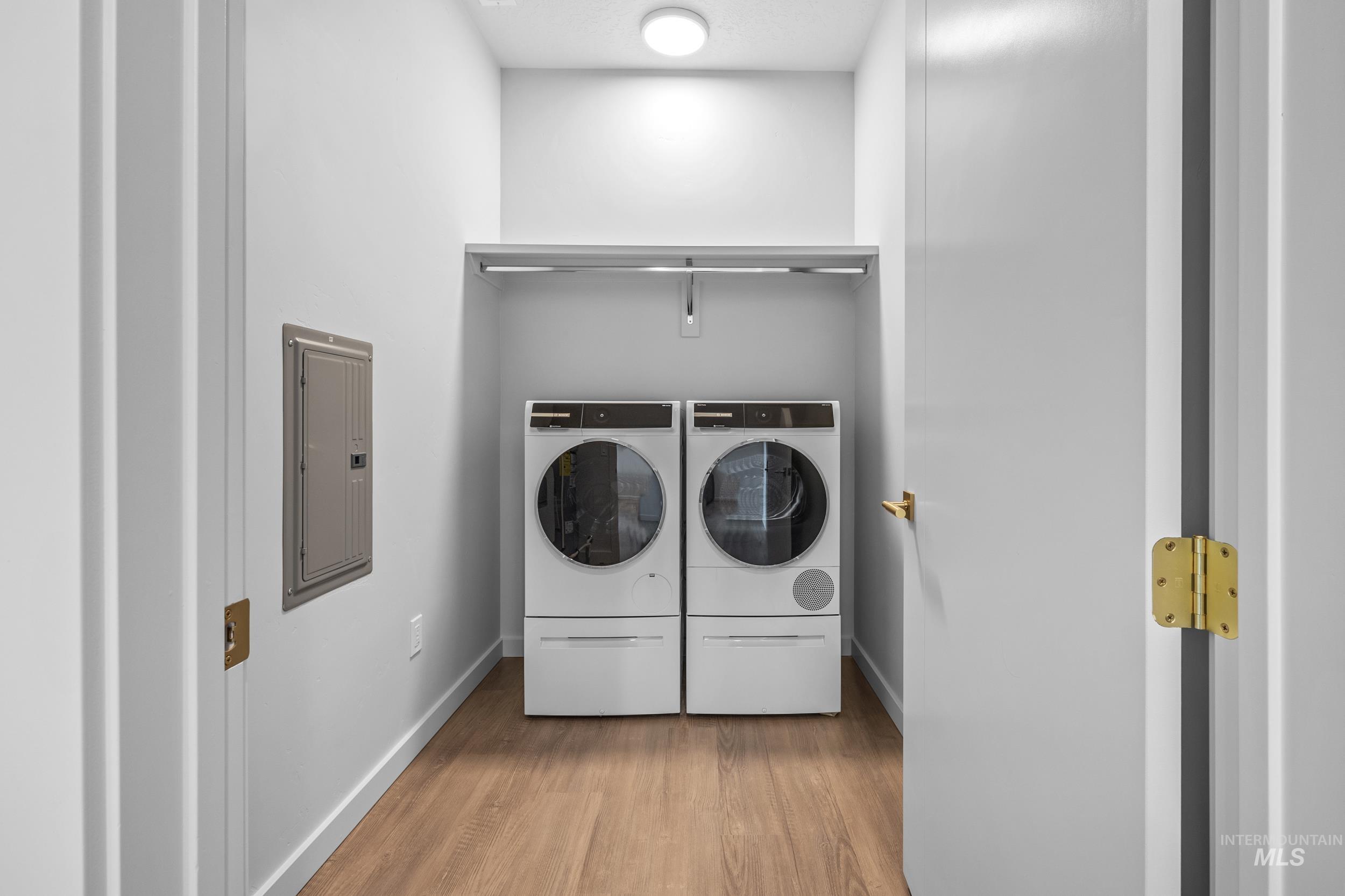 Laundry room featuring wood finished floors, electric panel, and washing machine and clothes dryer