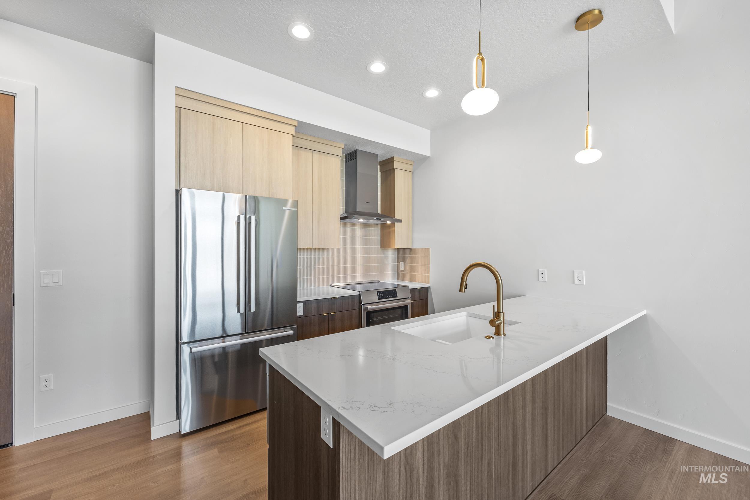 Kitchen featuring appliances with stainless steel finishes, modern cabinets, light stone countertops, decorative backsplash, and wall chimney range hood