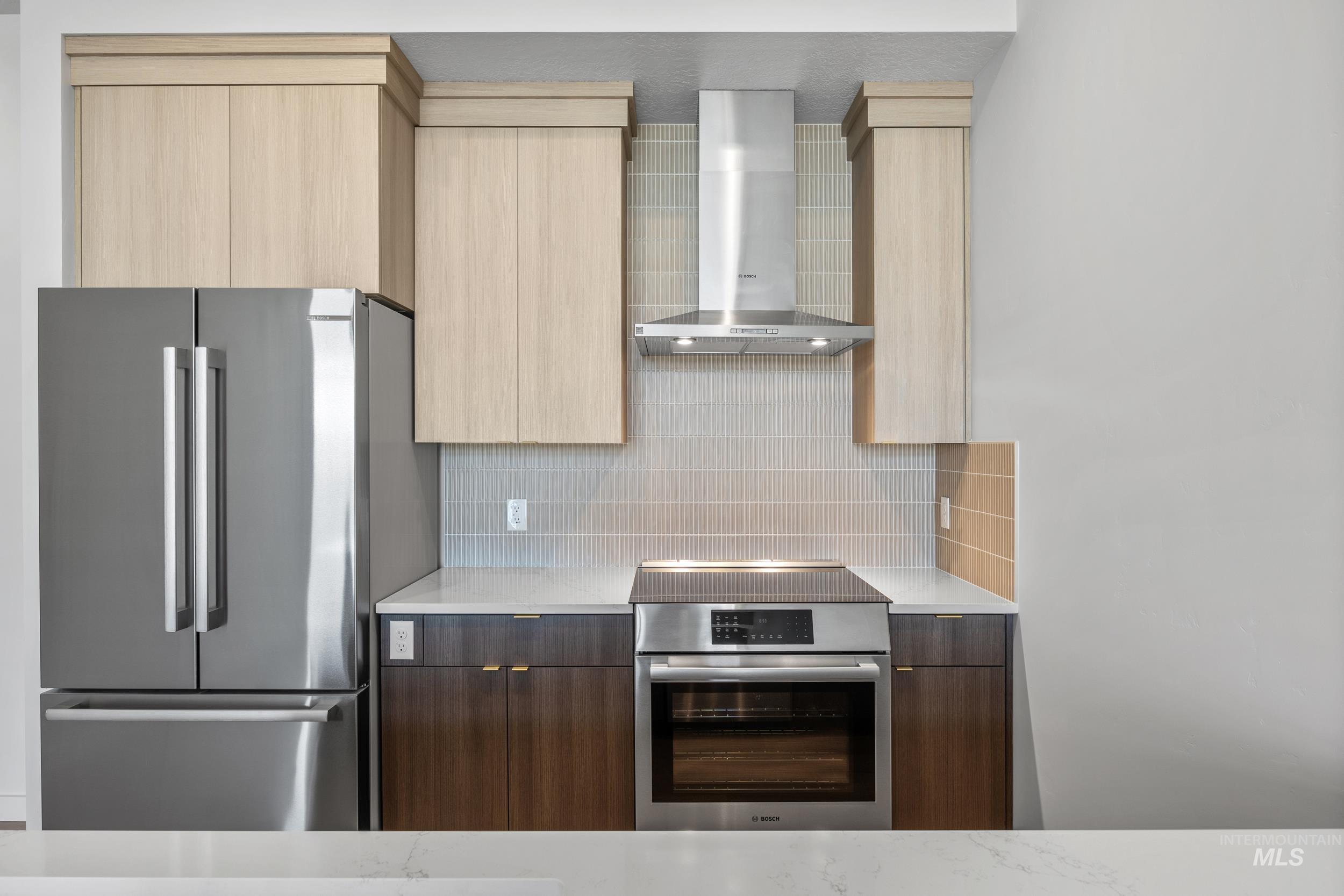 Kitchen featuring modern cabinets, appliances with stainless steel finishes, wall chimney range hood, and backsplash