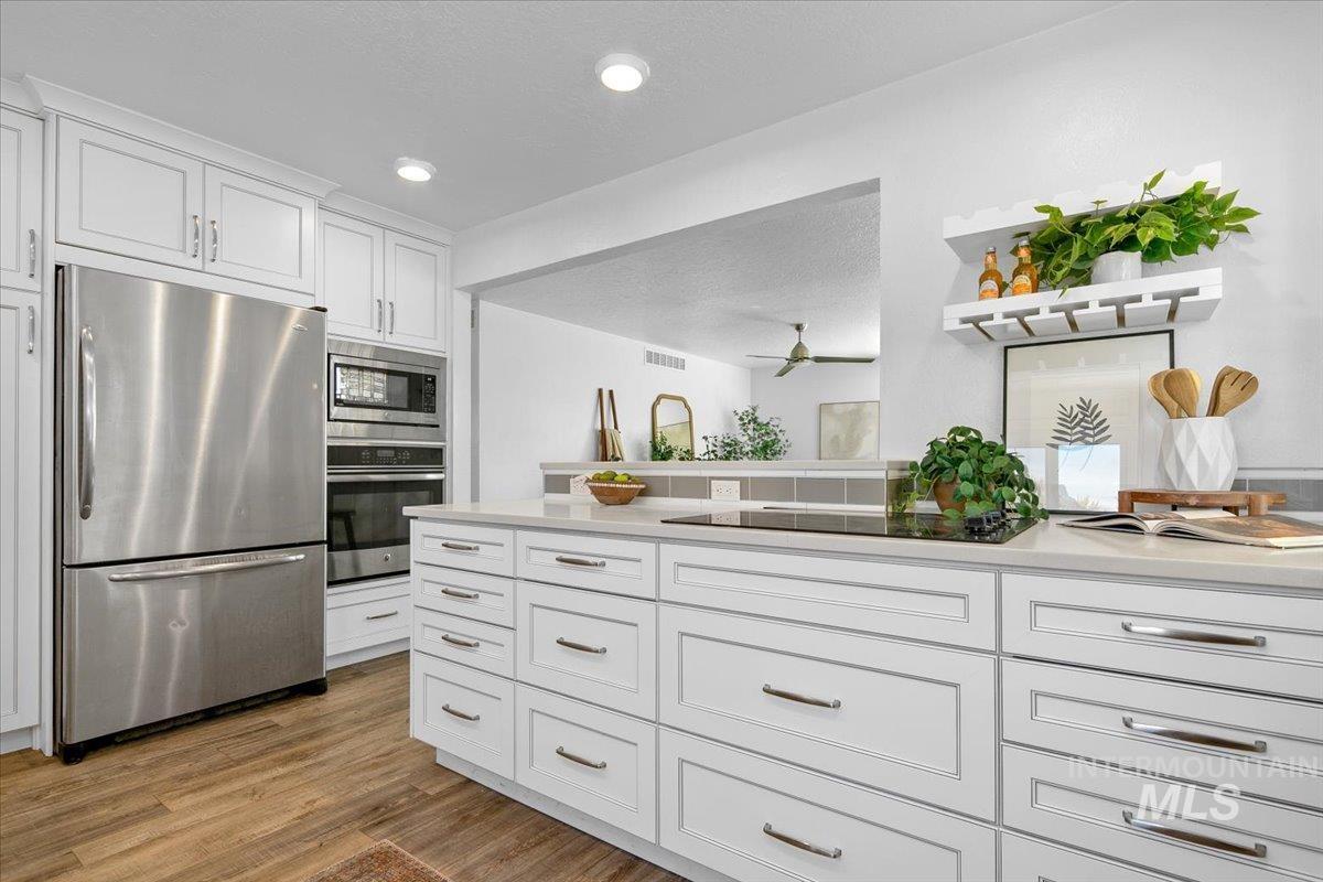 Kitchen with stainless steel appliances, white cabinets, open shelves, a textured ceiling, and light stone countertops