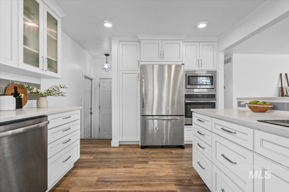 Kitchen featuring appliances with stainless steel finishes, white cabinets, dark wood-style flooring, light stone counters, and recessed lighting