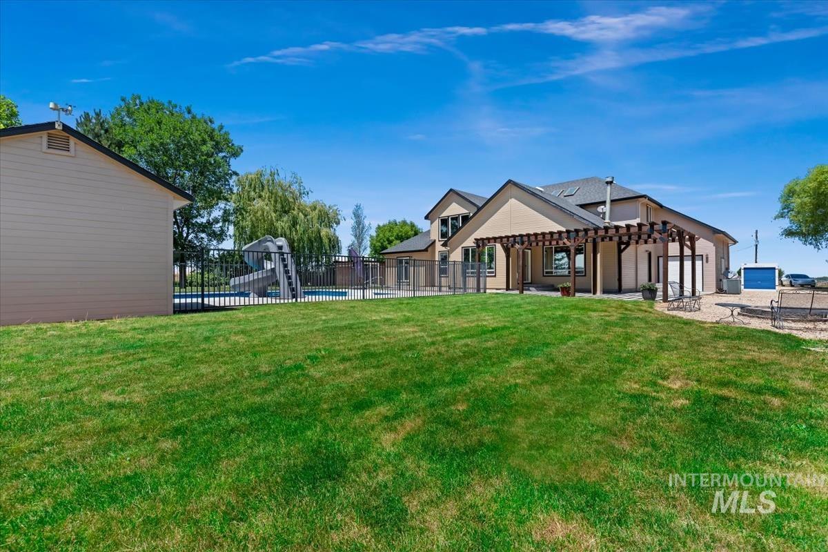 Expansive green lawn with a pergola-covered patio, fenced swimming pool, and detached storage shed