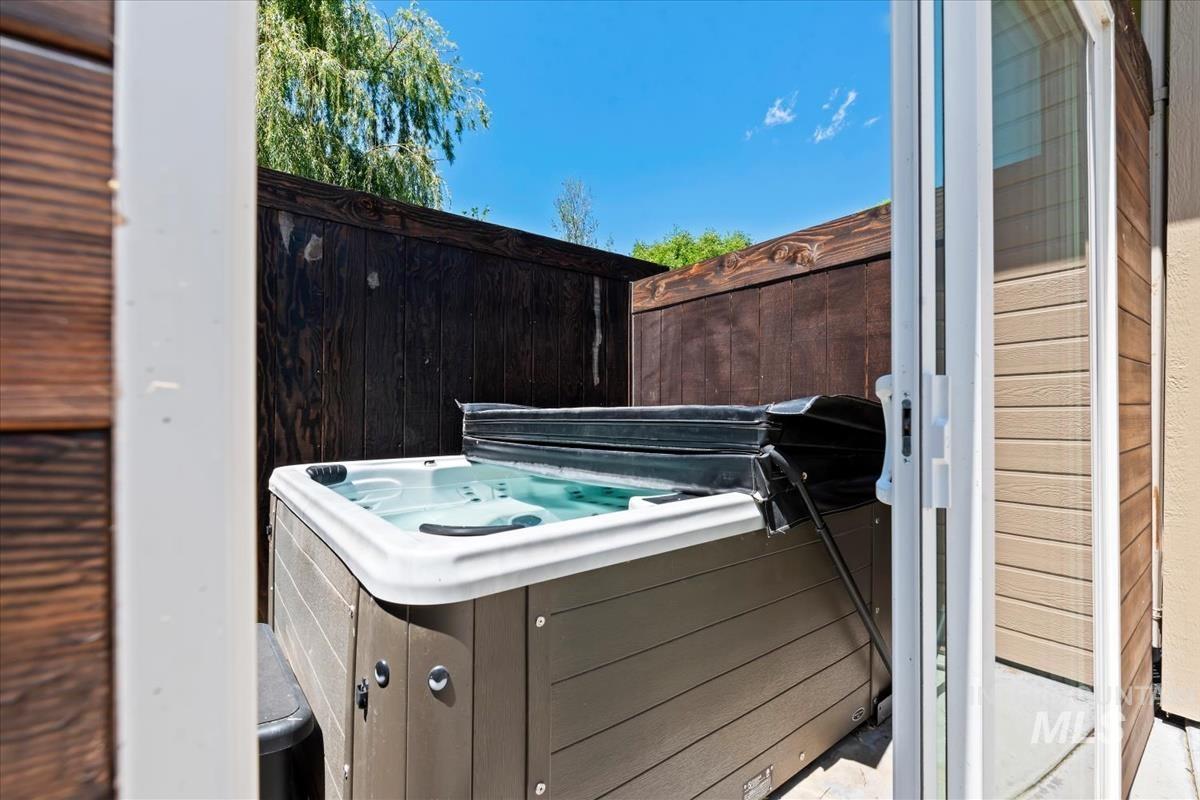 Outdoor spa with a partial cover on a paved patio, enclosed by a dark wood fence and accessible via a glass sliding door