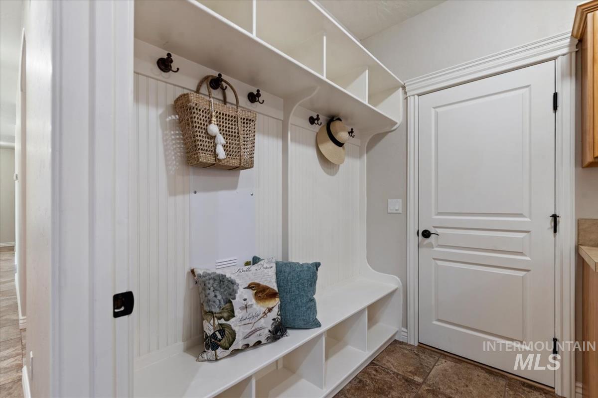 Built-in white storage unit featuring beadboard paneling, multiple coat hooks, and open shelving