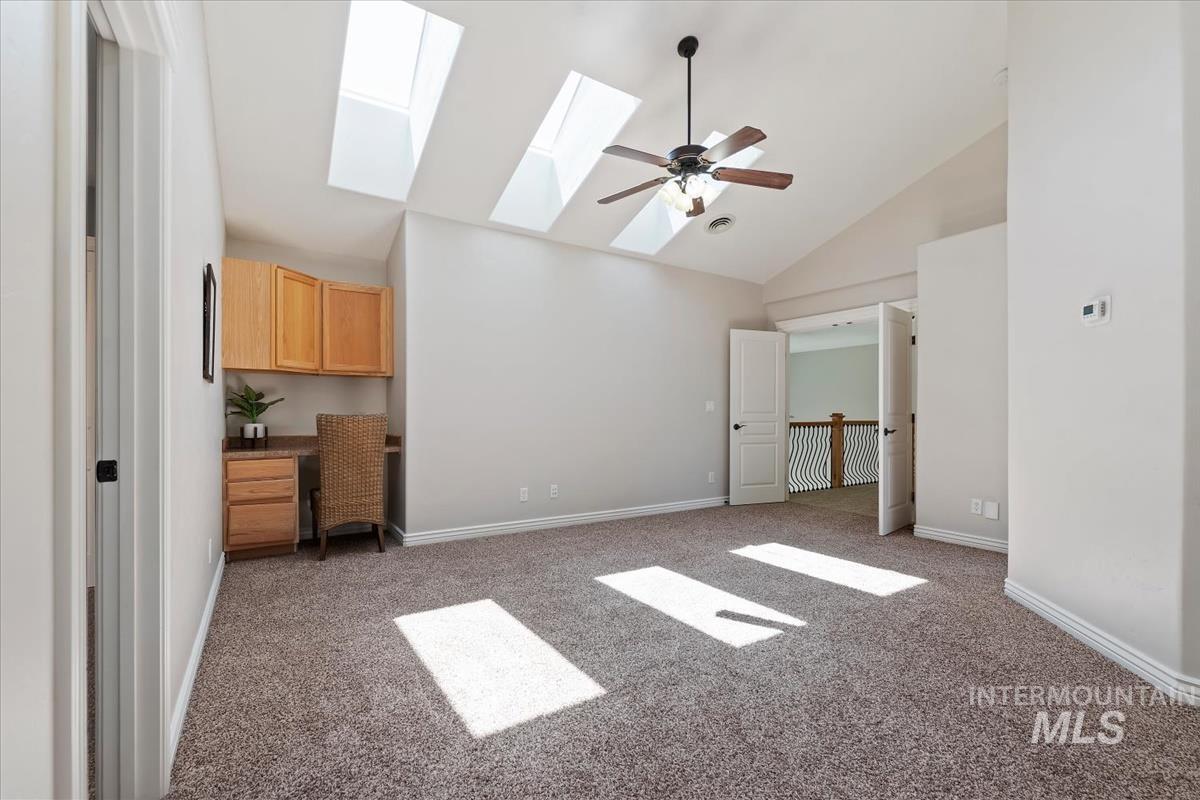 Spacious room featuring vaulted ceilings, multiple skylights, and a ceiling fan