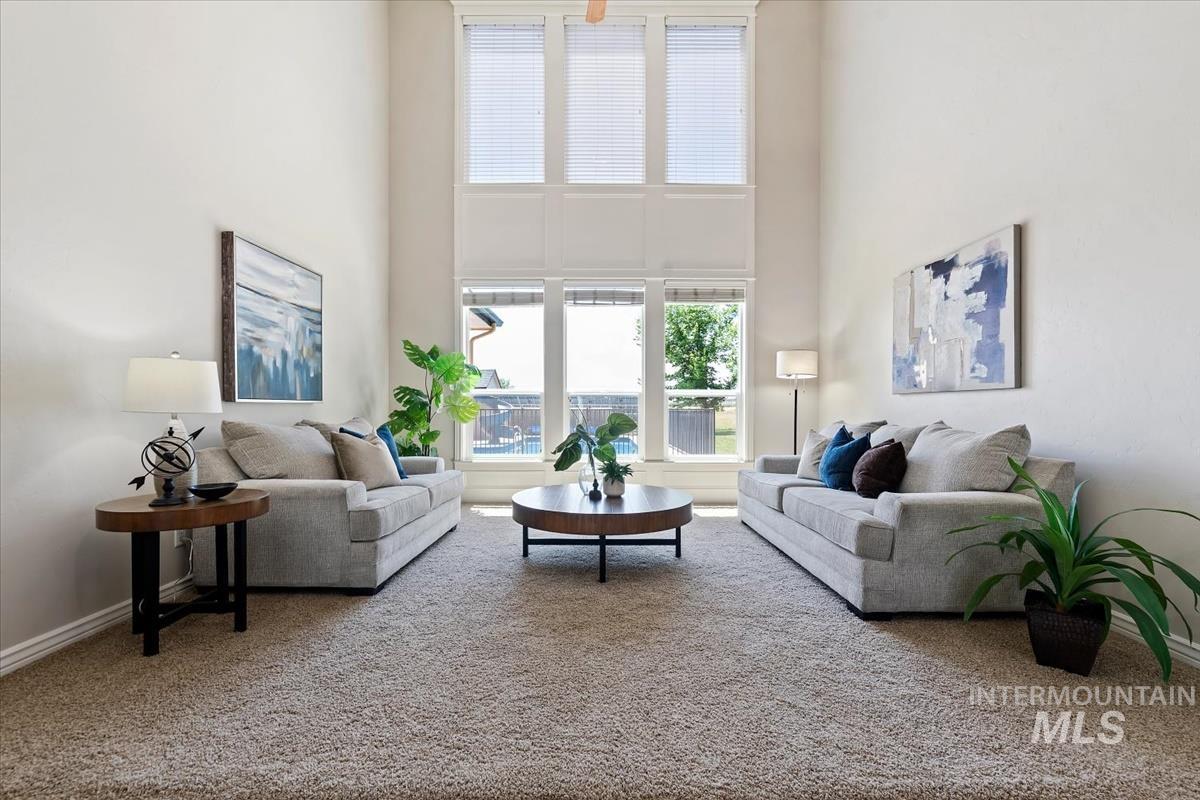 Living area featuring a two-story ceiling, tall windows with blinds, and neutral carpeting