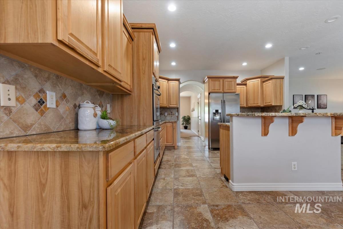 Kitchen featuring wood-finish cabinetry, stone tile flooring, granite-style countertops, mosaic tile backsplash, and recessed lighting