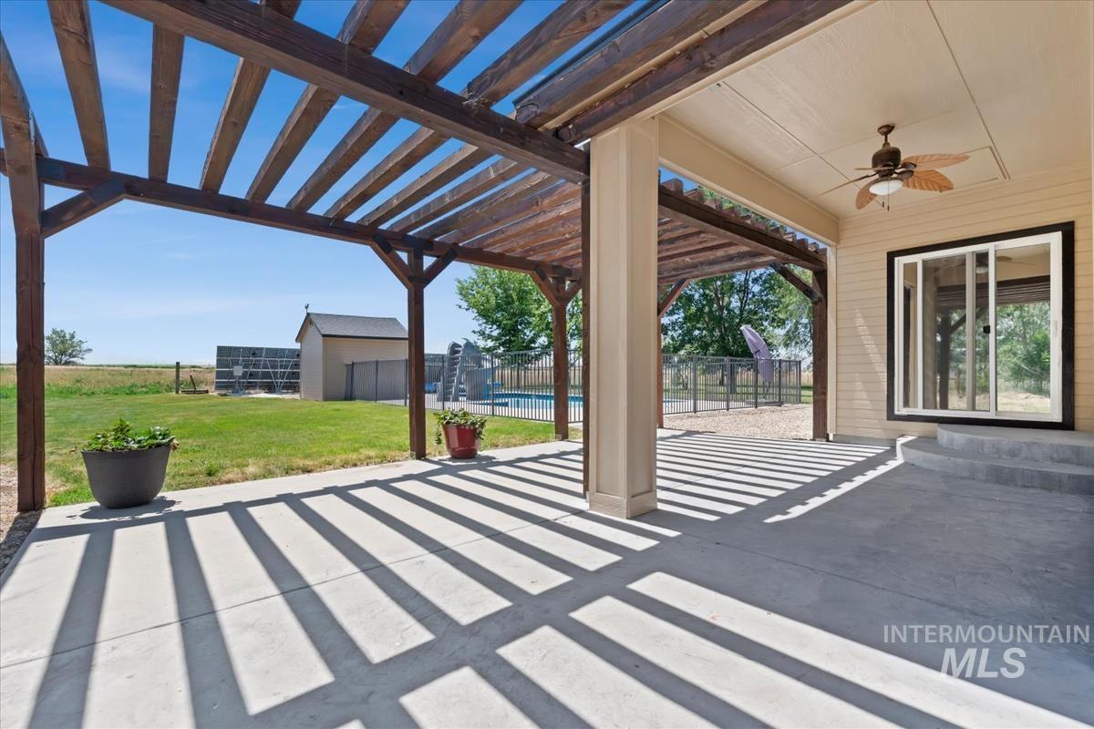 Expansive concrete patio featuring a wood pergola and a covered area with a ceiling fan
