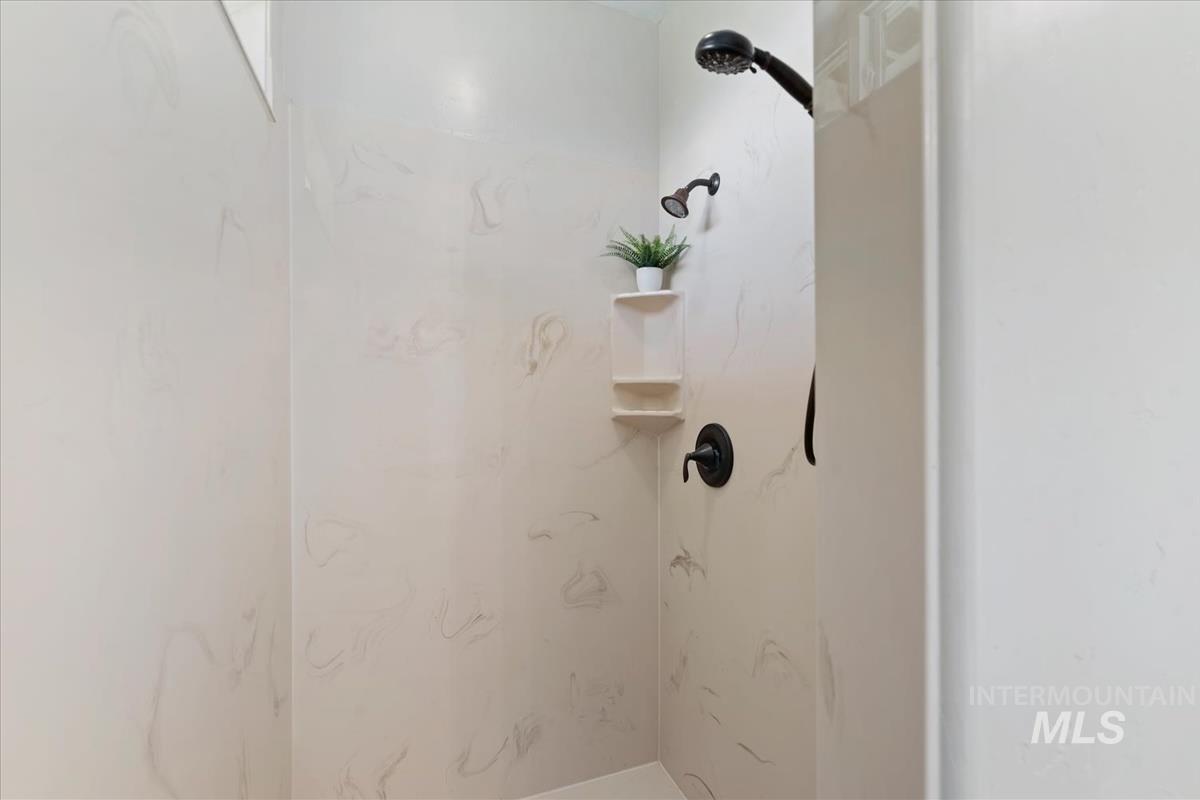 Shower enclosure featuring light-toned paneling with subtle veining, a matte black showerhead, and a matte black single-handle shower valve