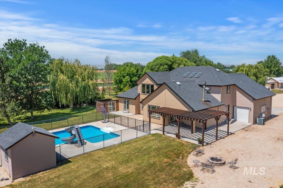 Expansive backyard featuring a fenced swimming pool, fire pit area, and a large wooden pergola