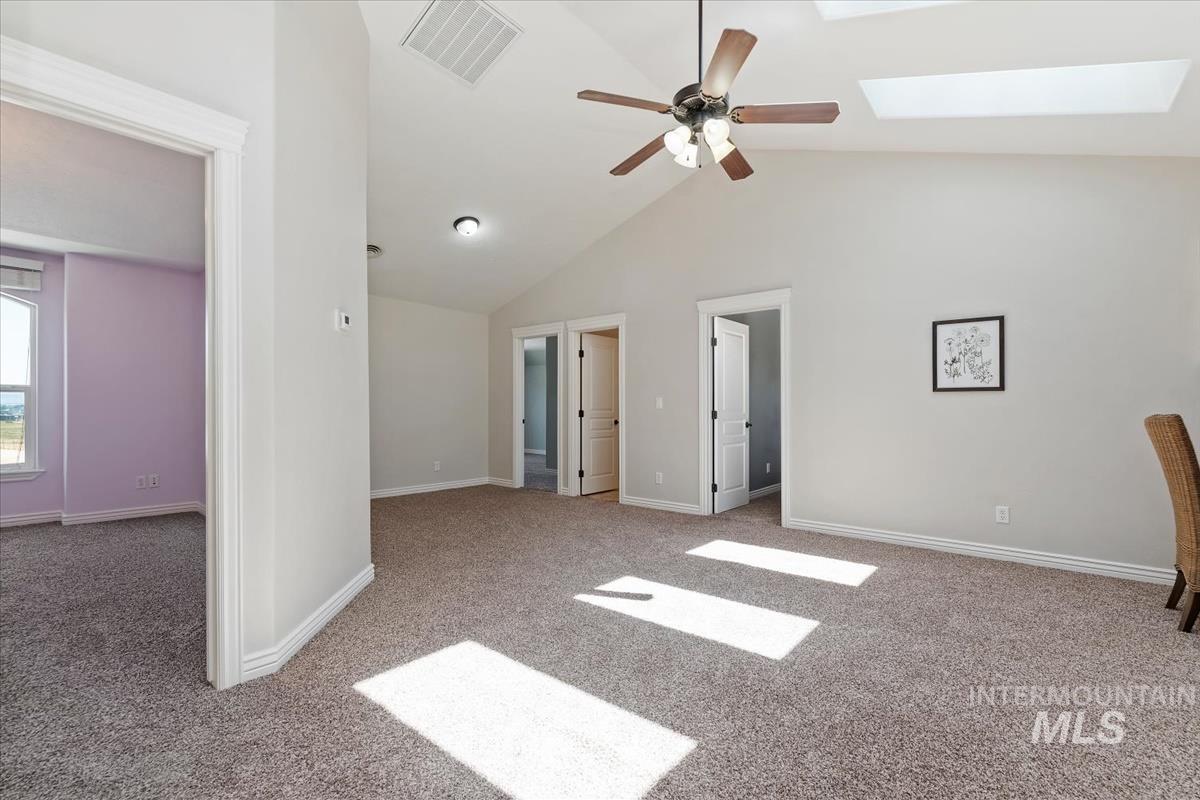 Spacious carpeted room featuring a vaulted ceiling with a ceiling fan, a skylight, and multiple interior doorways